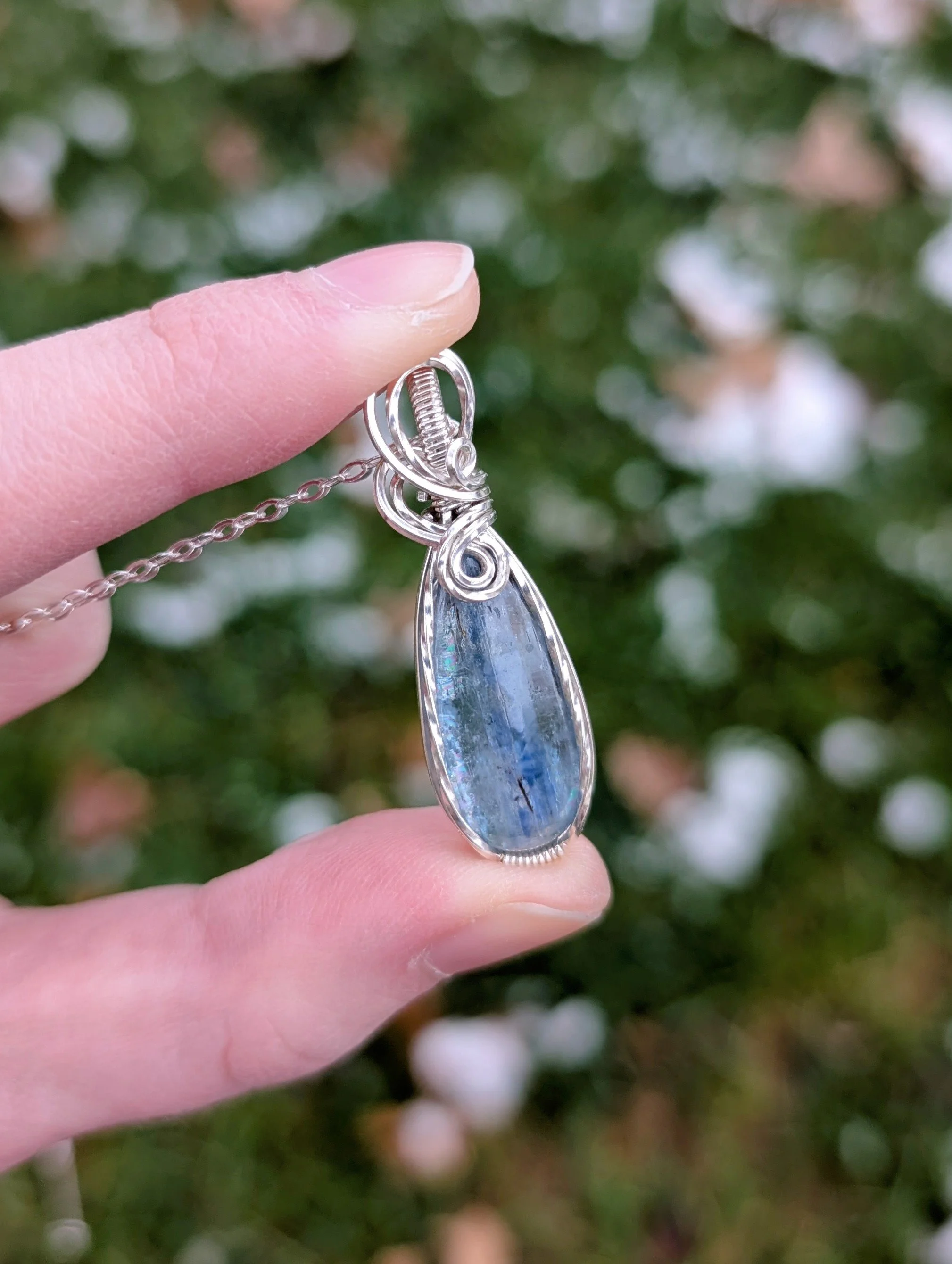 A pendant necklace made from a teardrop shaped icy kyanite stone set in sterling silver wire held tilted to the side.. It has a sterling silver chain.