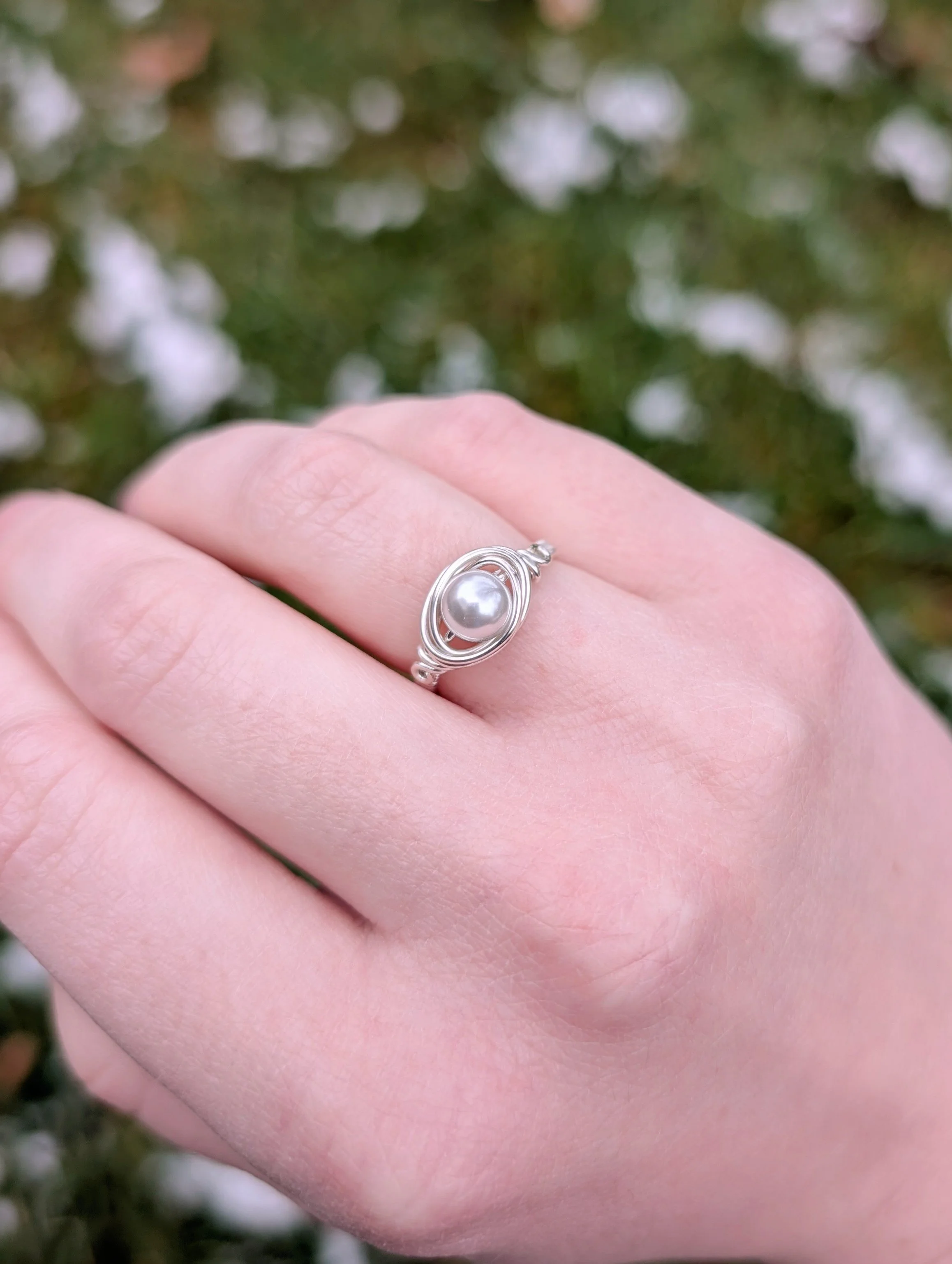 a wire wrapped ring made from a white glass pearl and sterling silver wire worn on the ring finger of the model's right hand.