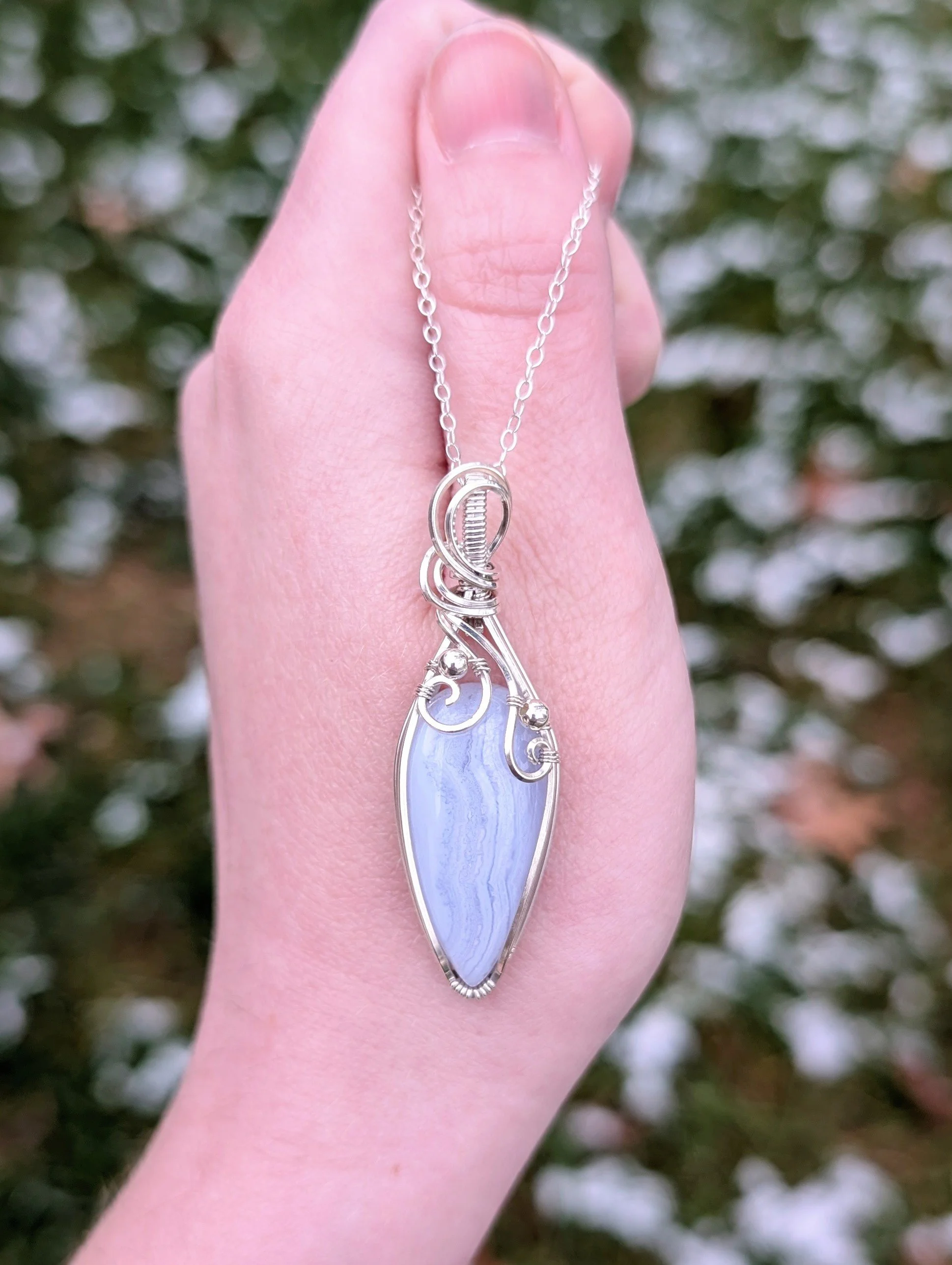 Pendant made with a teardrop-shaped blue lace agate stone wrapped in sterling silver with swirls and bead details