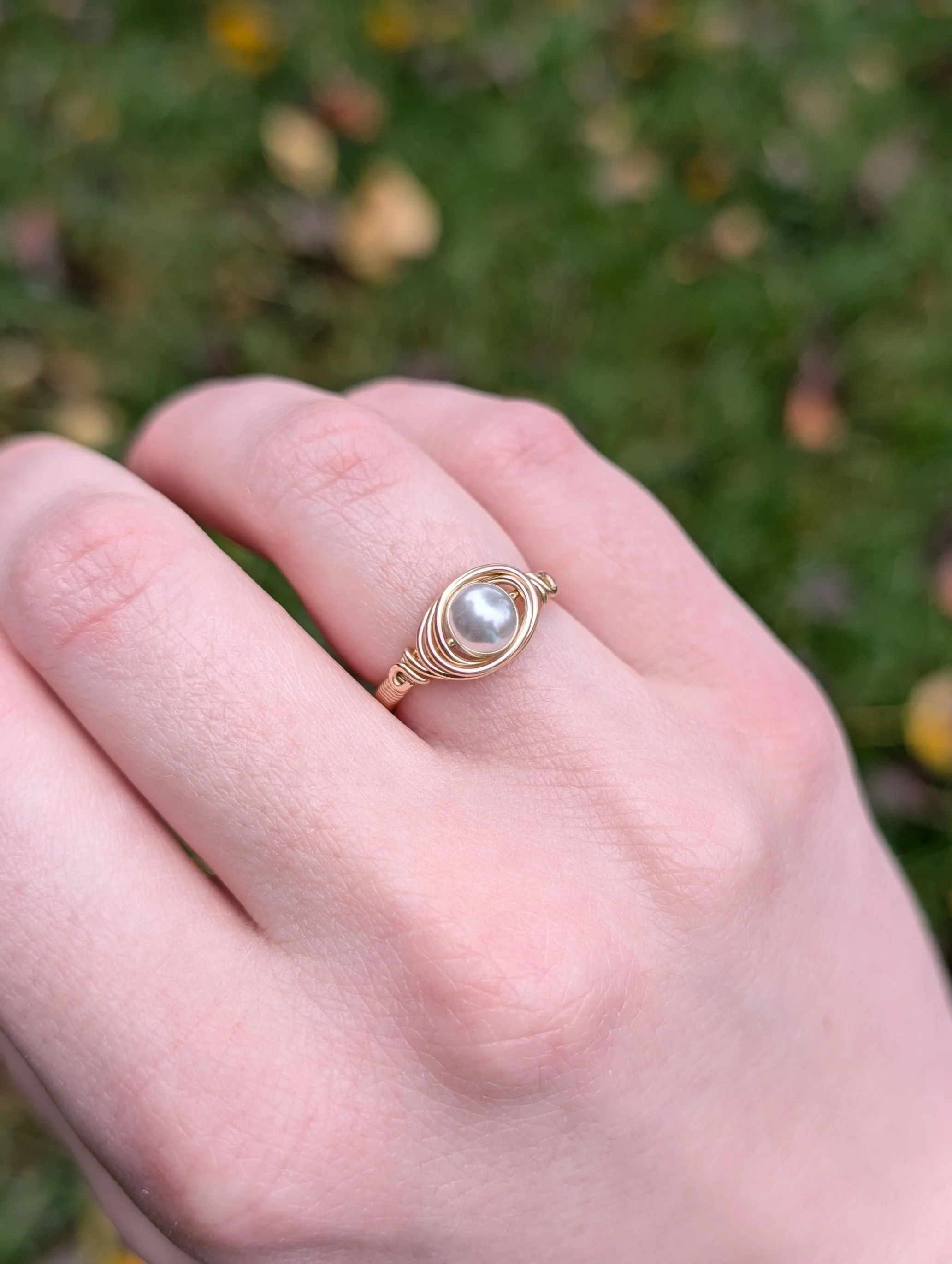 a wire wrapped ring made from a white glass pearl and gold filled wire worn on the ring finger of the model's right hand..