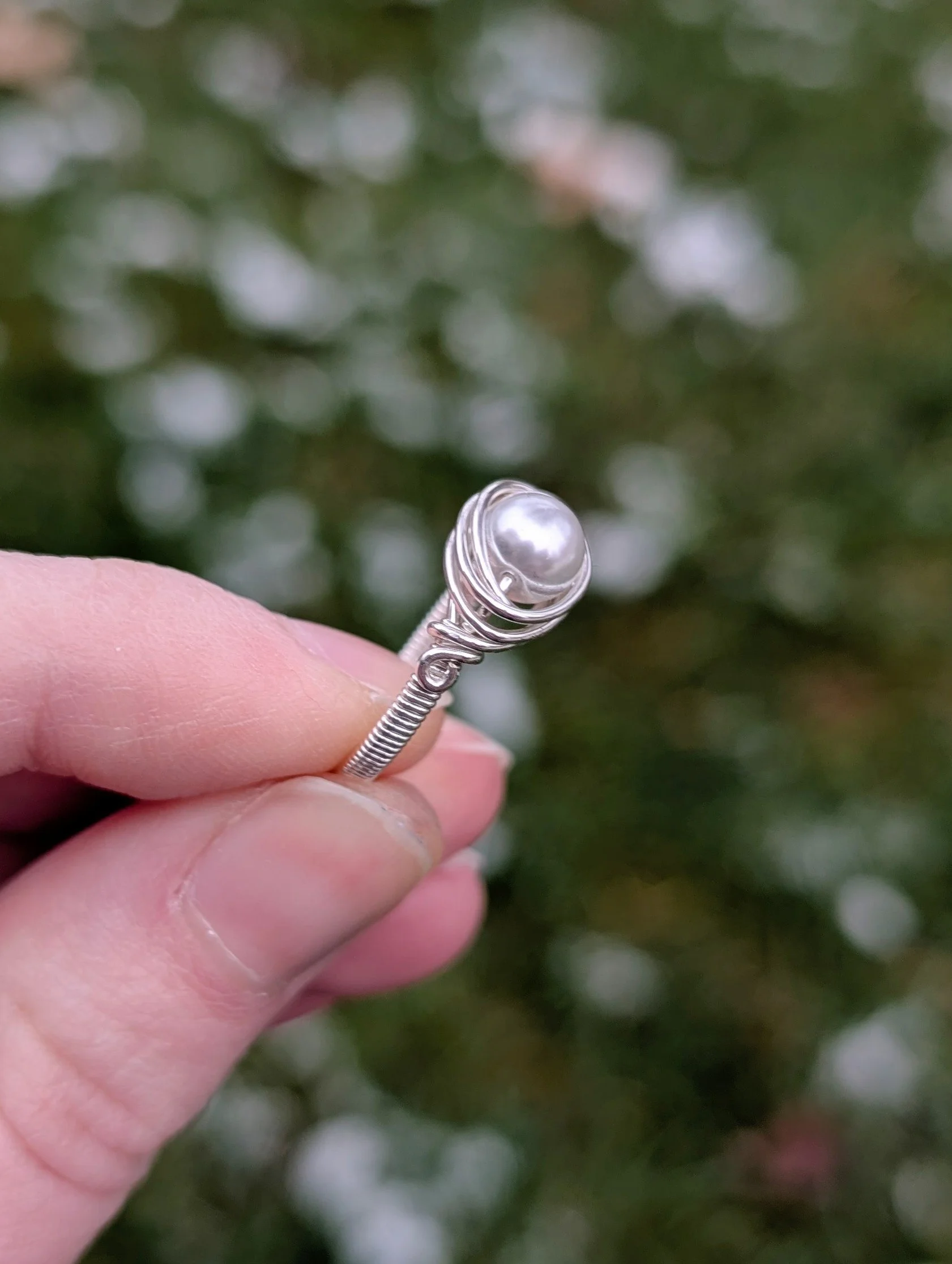 a wire wrapped ring made from a white glass pearl and sterling silver wire held up between two fingers to show the side of the top of the ring.