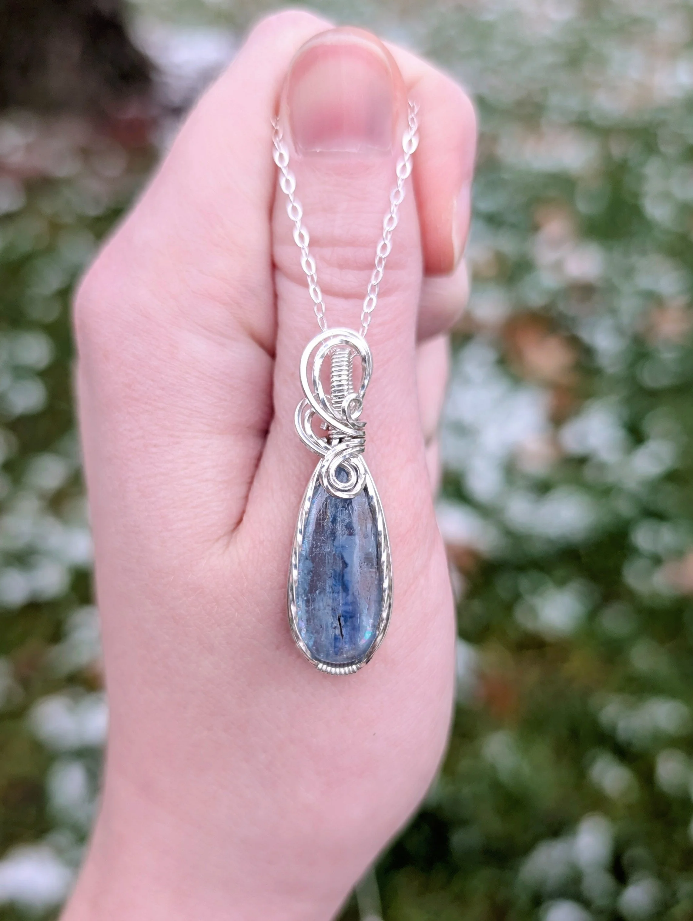 A pendant necklace made from a teardrop shaped icy kyanite stone set in sterling silver wire. It is hanging from a sterling silver chain.