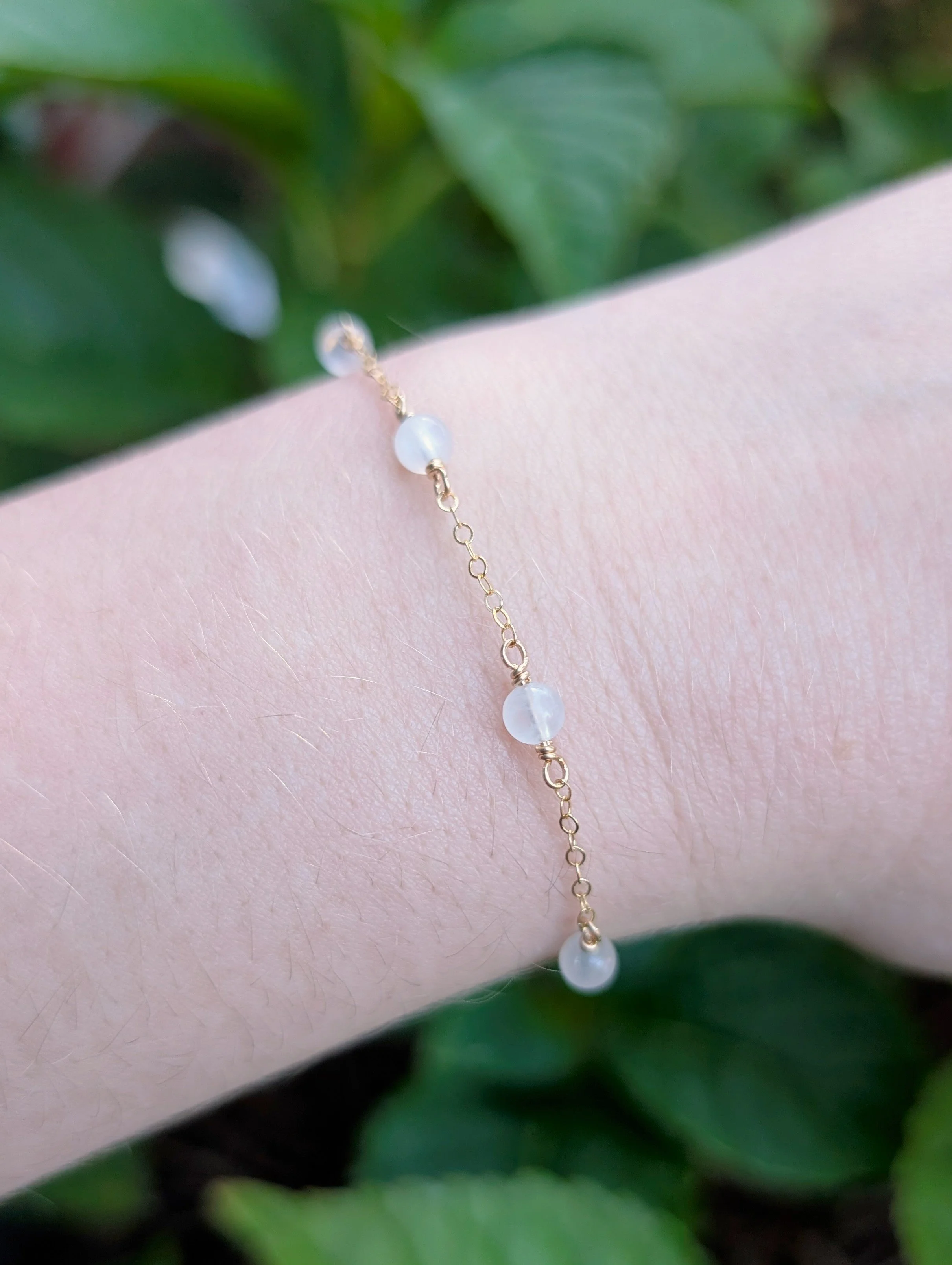 a dainty bracelet made with round moonstone beads and gold chain. Featured on a model's wrist.
