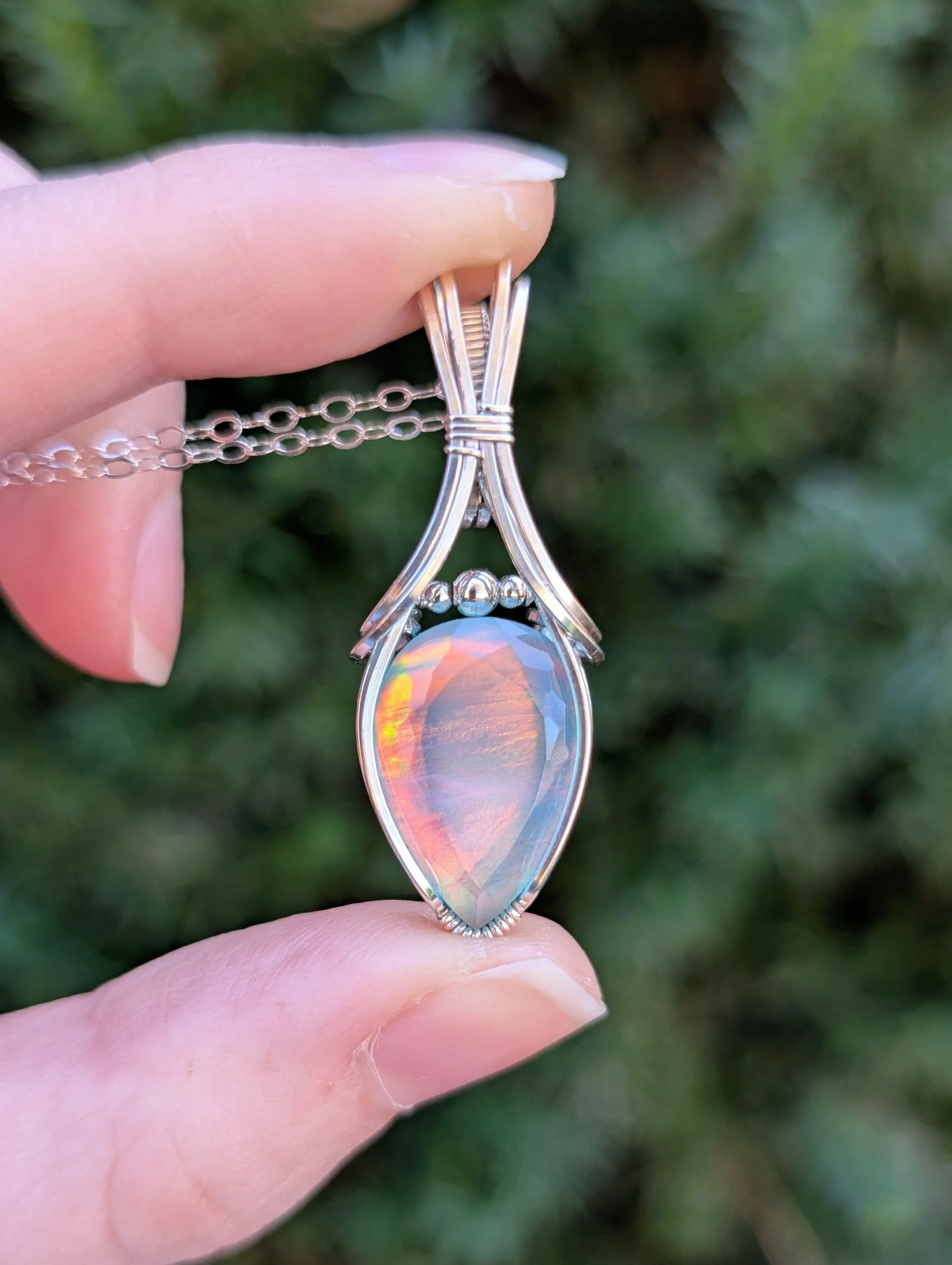 The vaeloria necklace in soft light. Features a teardrop aurora opal stone wrapped in sterling silver wire.