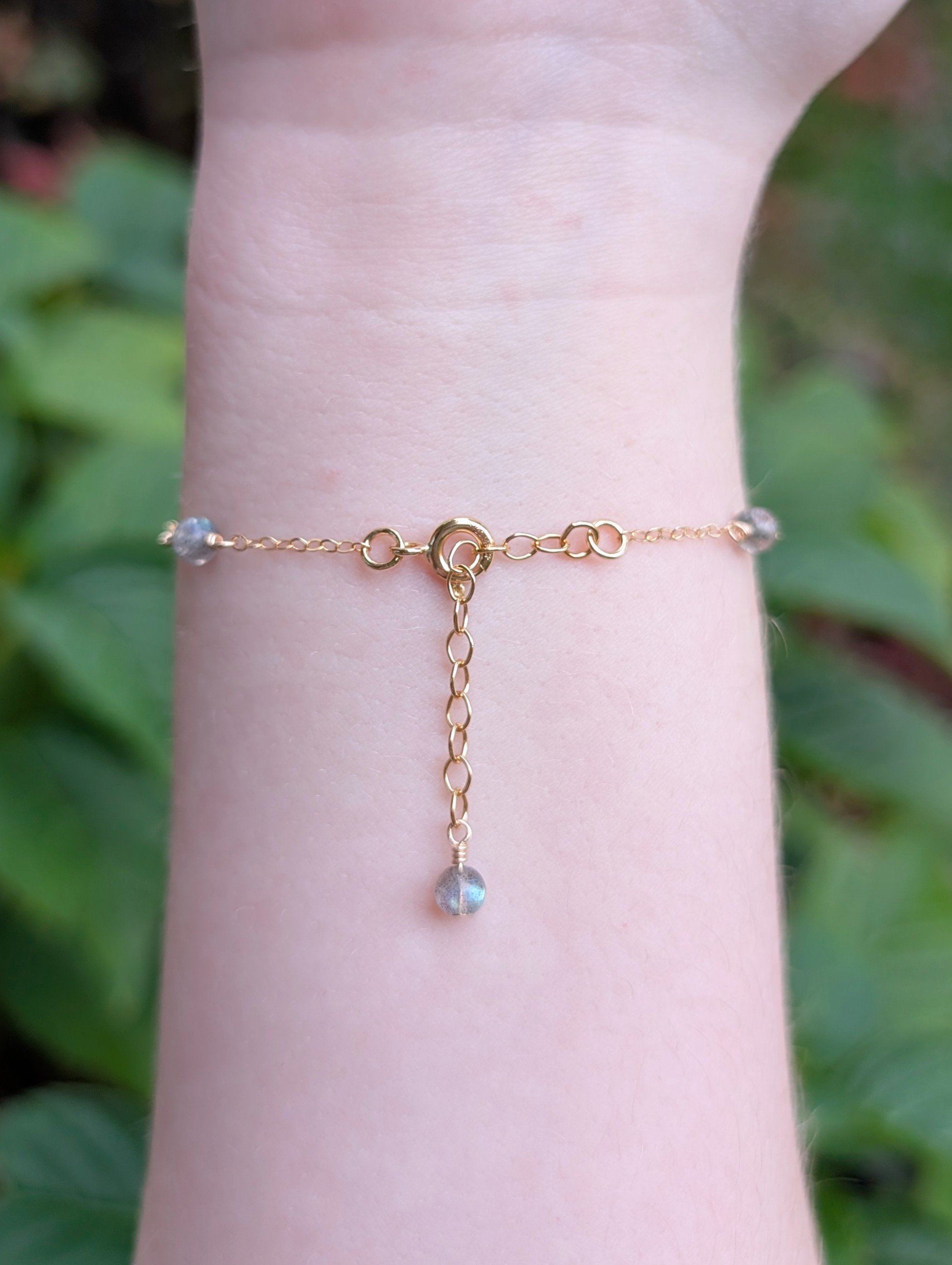 a bracelet made with round labradorite beads and gold chain. Featured on a model's wrist showing the clasp and extension chain.