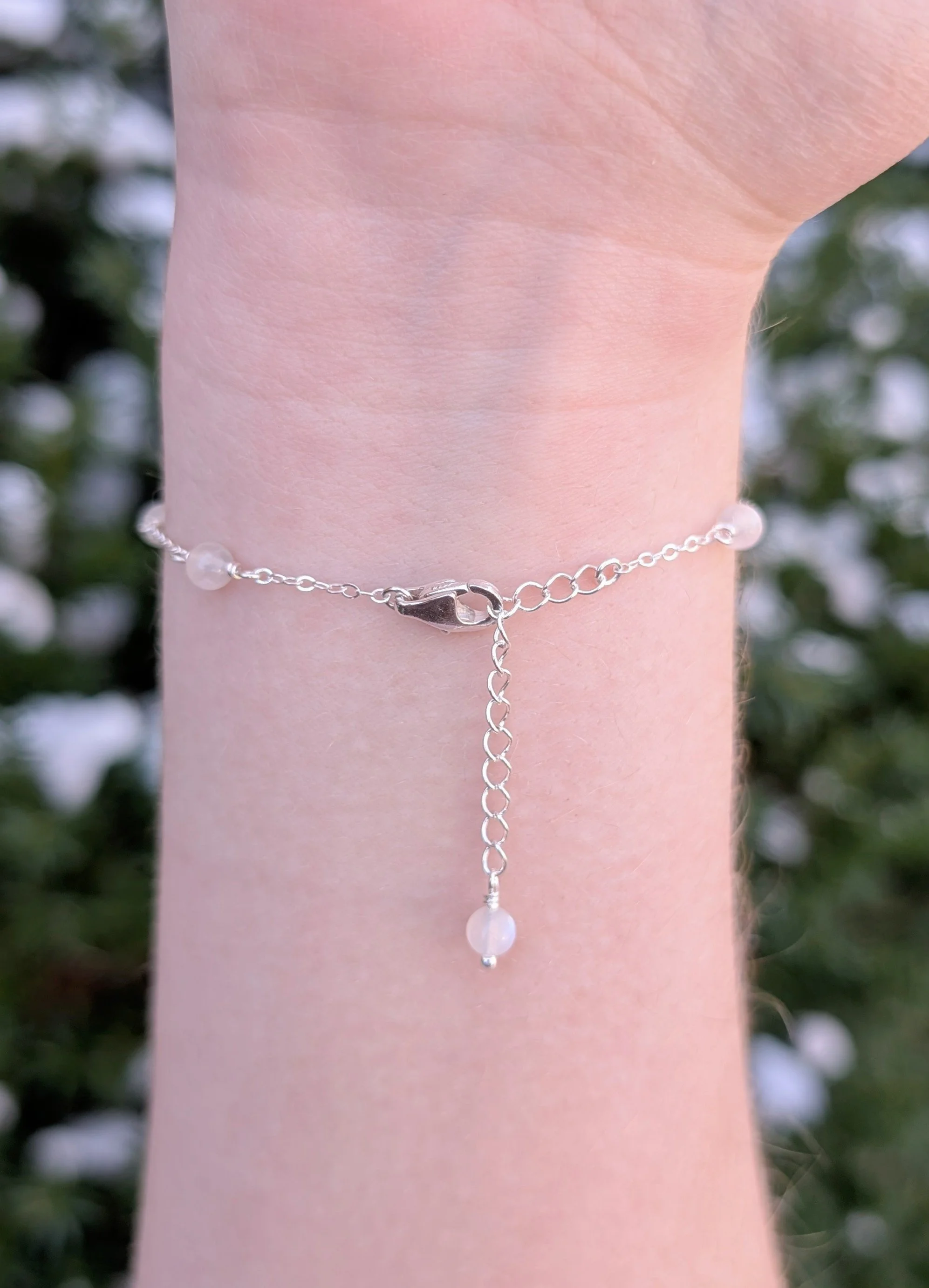 Bracelet made with white moonstone beads and sterling silver chain modeled on wrist, showing the clasp and extension chain.