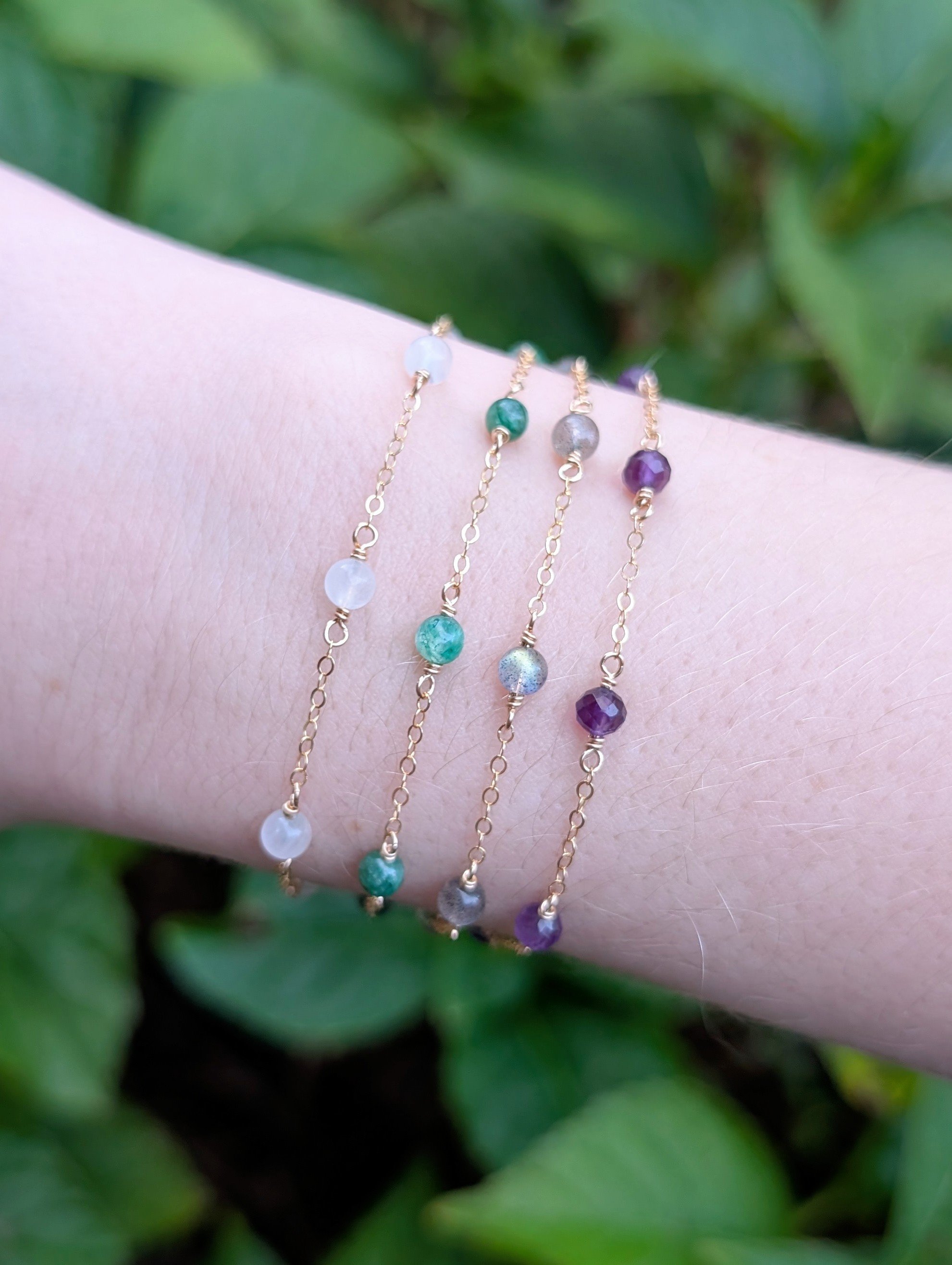 Four dainty gemstone pendants made with white, green, gray, and purple stones and 14k gold filled chain