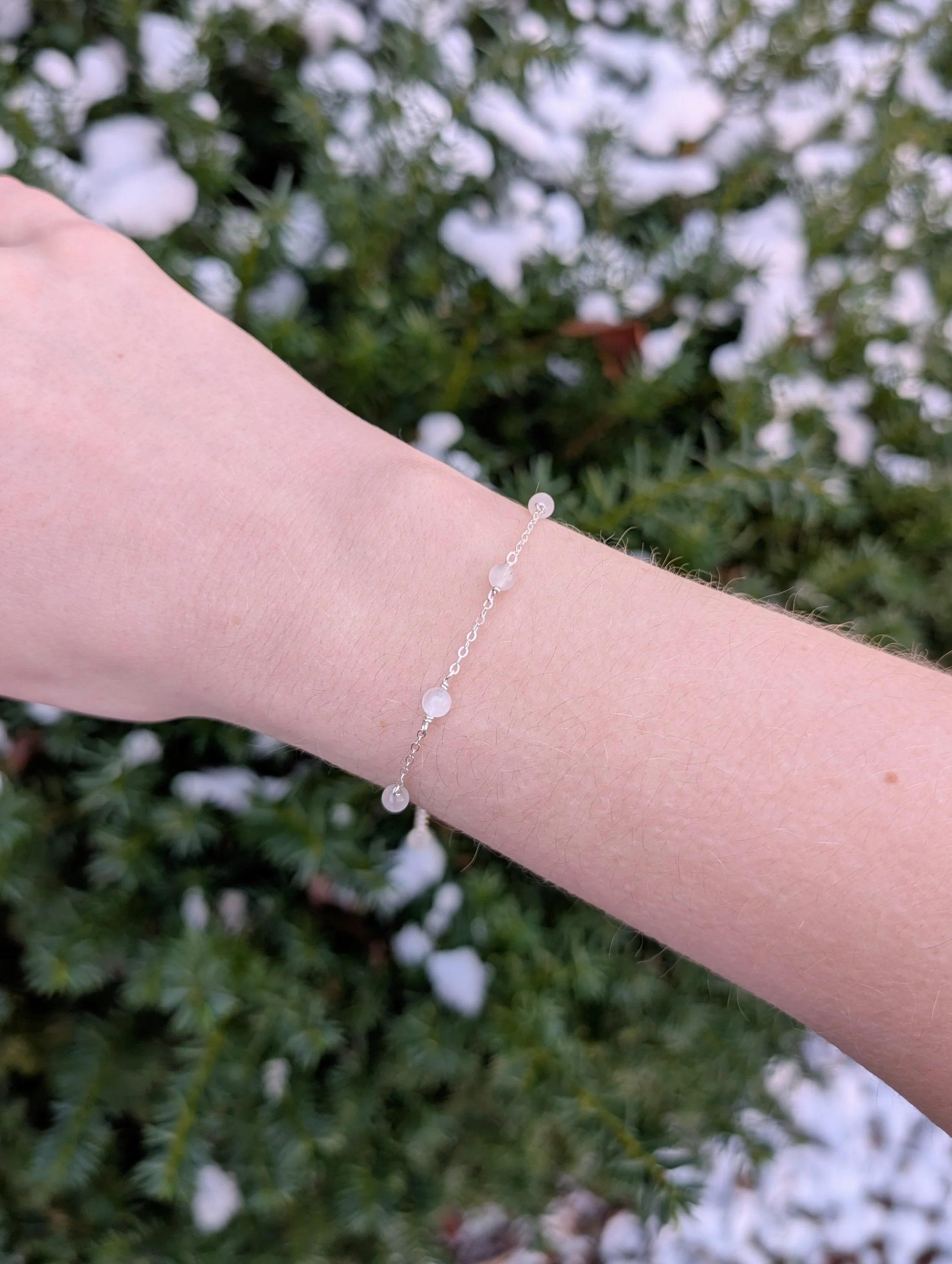 Bracelet made with white moonstone beads and sterling silver chain modeled distantly on wrist.
