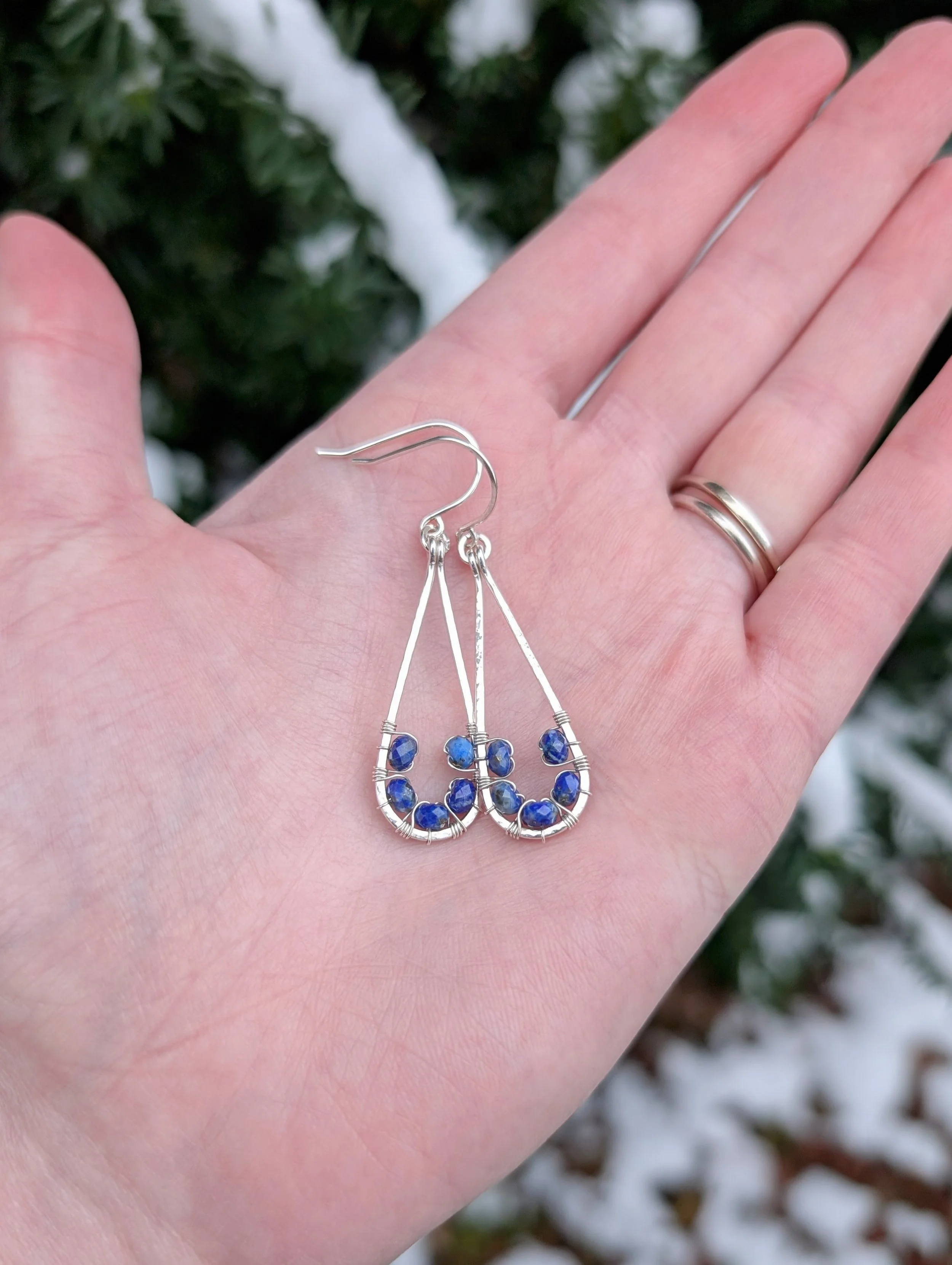 The Cobalt Sky Earrings are being held in the palm of a model's hand showing the front of the earrings. They are made with lapis lazuli beads and sterling silver wire.