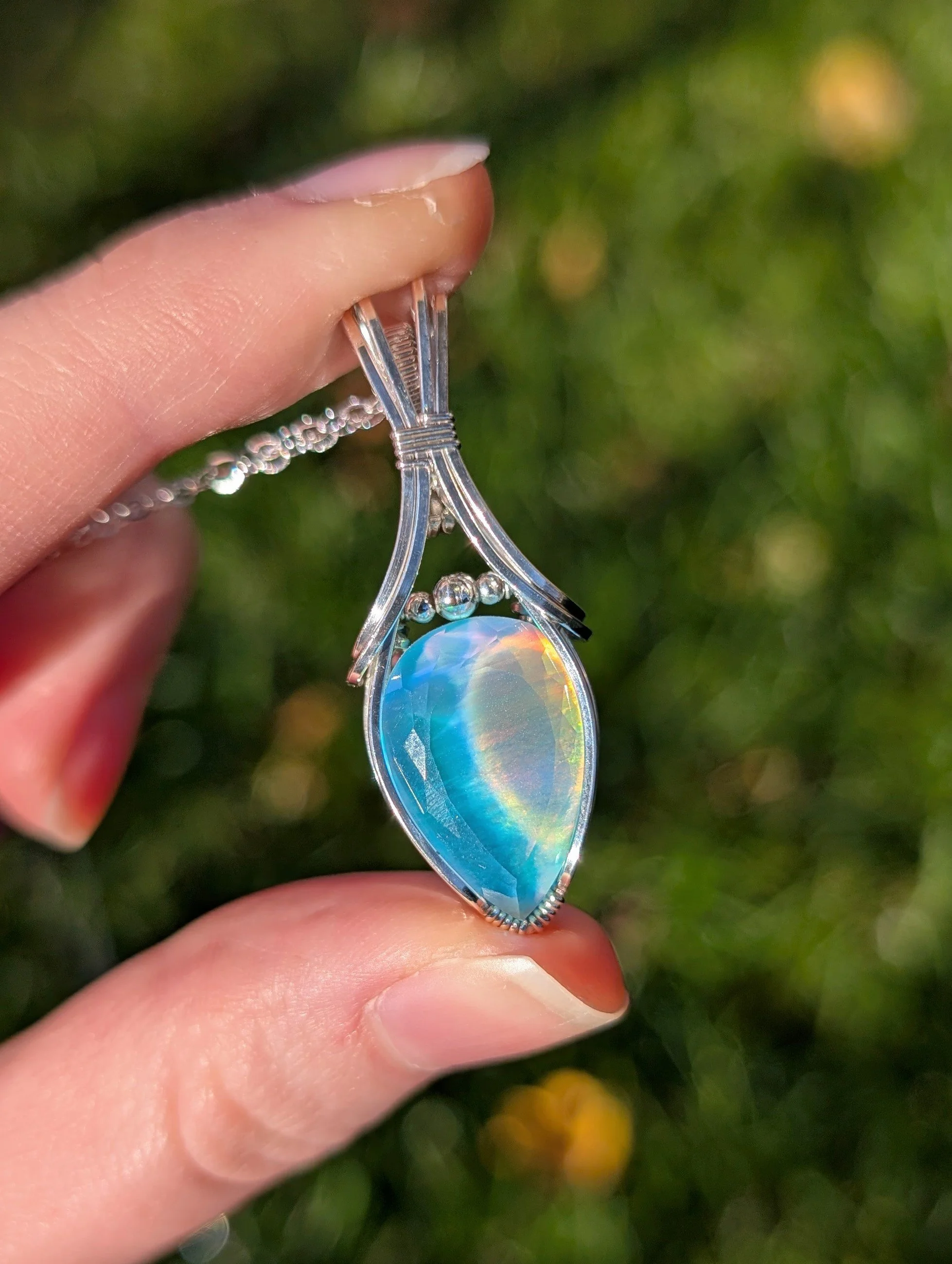 The vaeloria necklace in direct sunlight. Features a teardrop aurora opal stone wrapped in sterling silver wire.