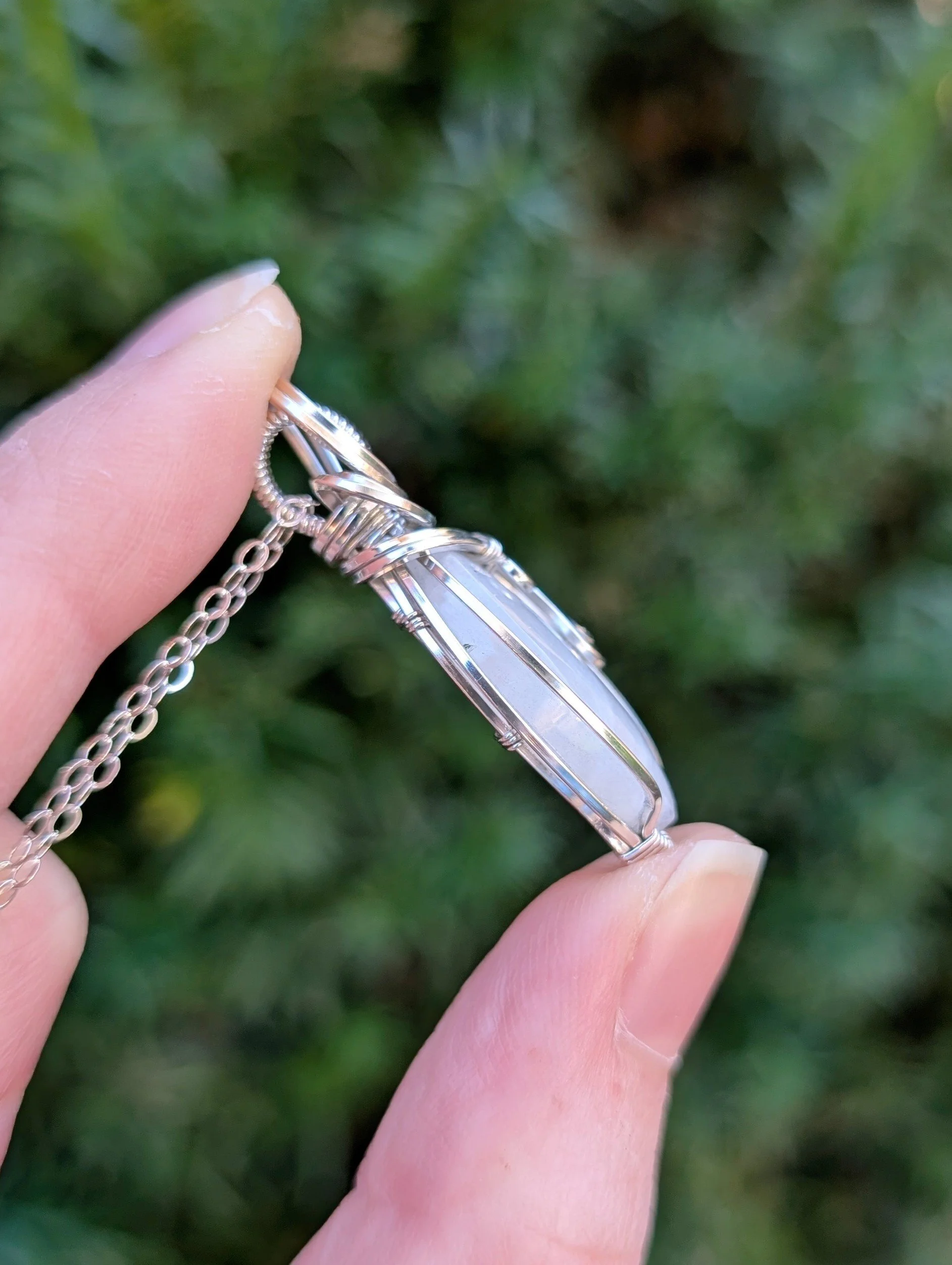 The side of a marquis-shaped rainbow moonstone pendant wrapped in sterling silver.