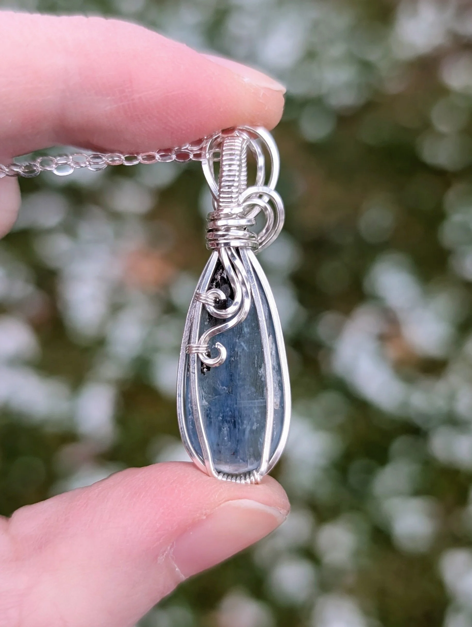 The back of a pendant necklace made from a teardrop shaped icy kyanite stone set in sterling silver wire. It has a sterling silver chain.
