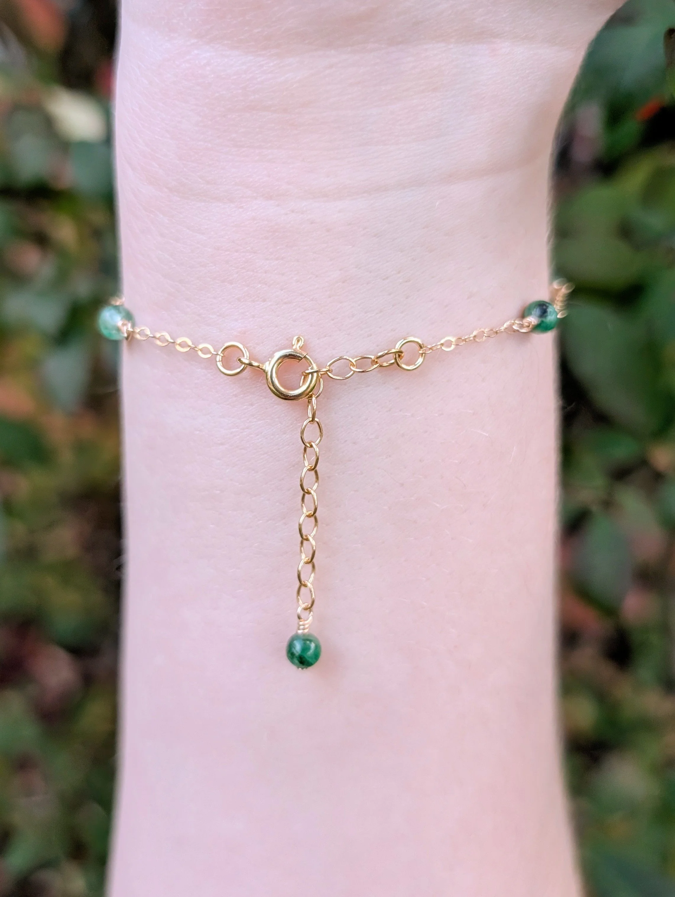 a bracelet made with round green apatite beads and gold chain. Featured on a model's wrist showing the clasp and extension chain.