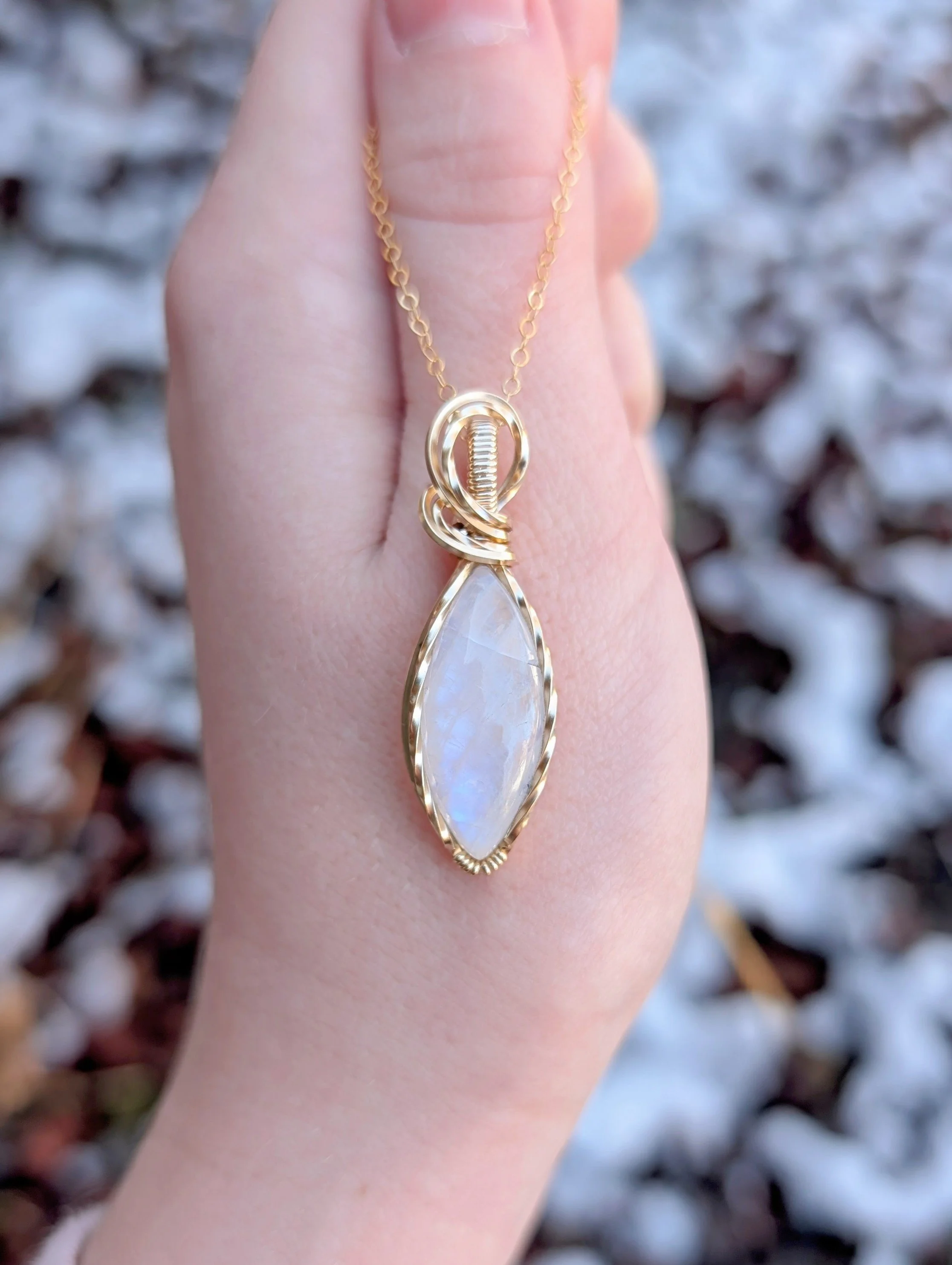A pendant made with a marqui-shaped moonstone and 14k gold filled wire hanging from a gold chain..