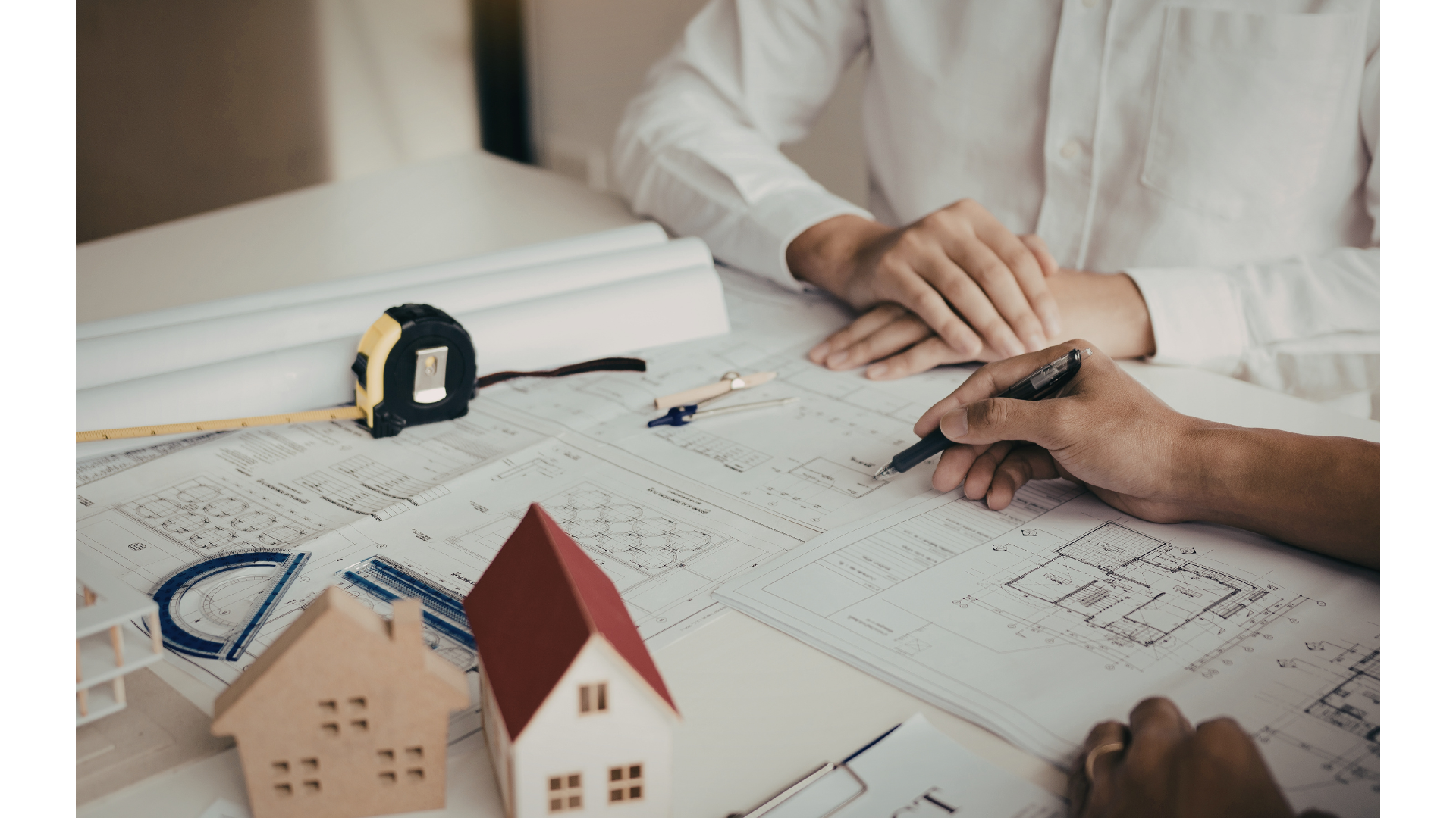 Architects reviewing blueprints and architectural models on a desk with tools and scaled models of houses.