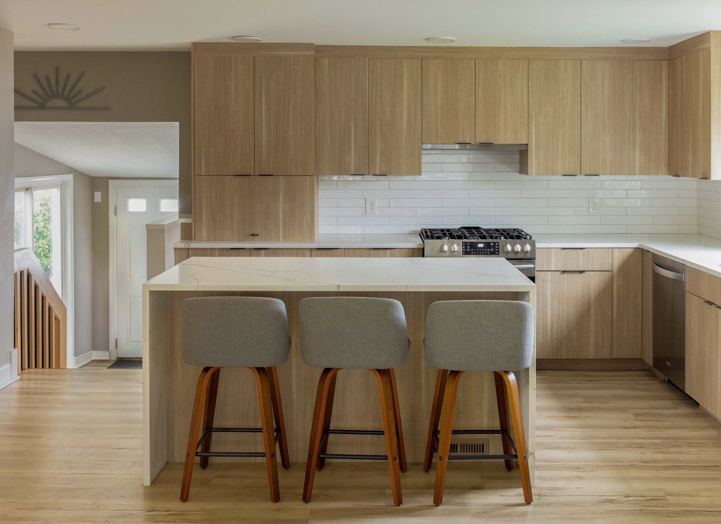 A newly renovated kitchen with oak flooring, light wood cabinets, and a kitchen island with three chairs.
