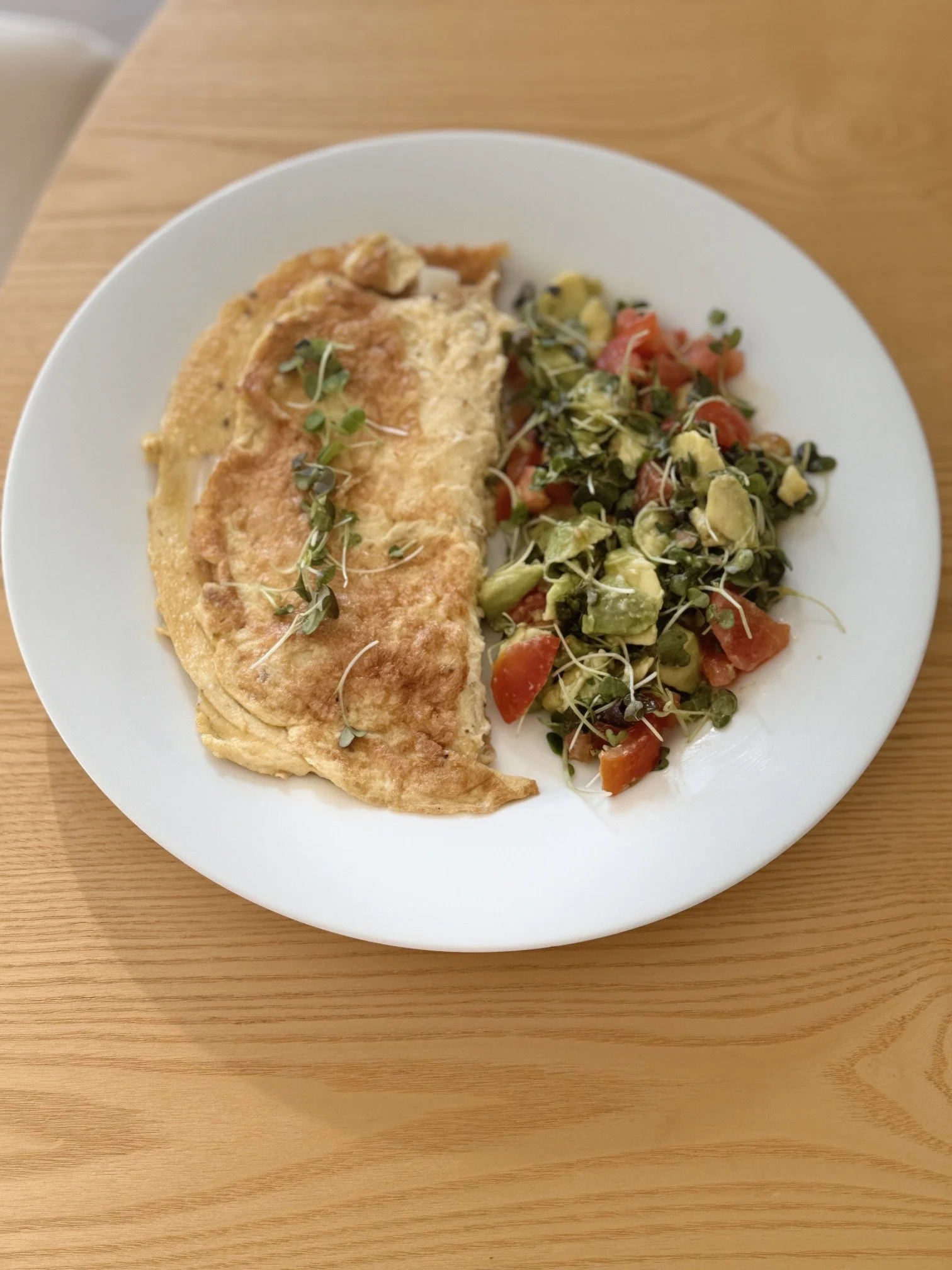 Omelette with a tomato, avocado and microgreen salad on a white plate