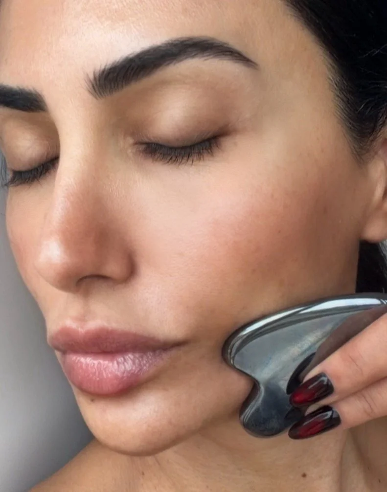 Sydney Sajadi using a gua sha stone along her jaw, eyes closed