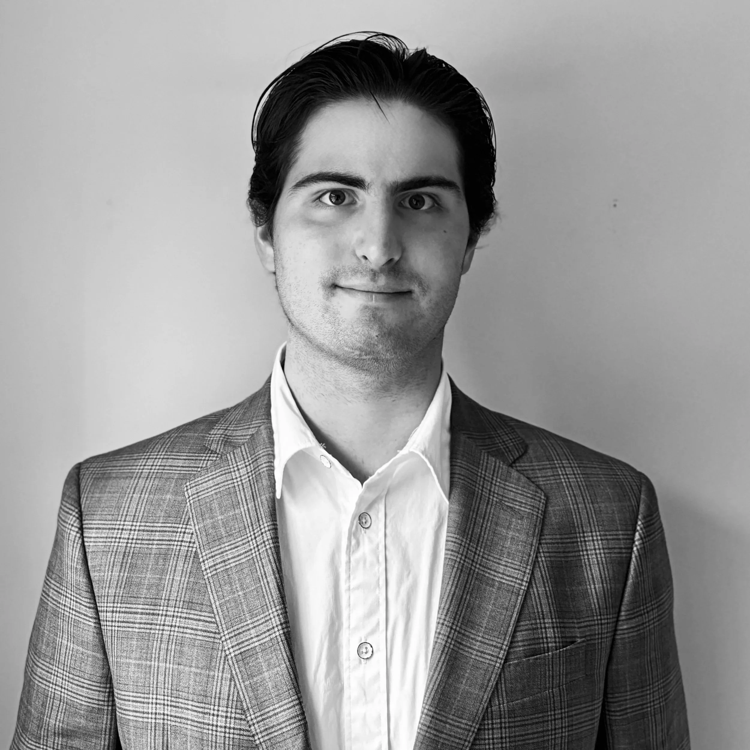 Black and white portrait of a young man with dark hair, wearing a checked blazer over a white shirt, against a plain background.