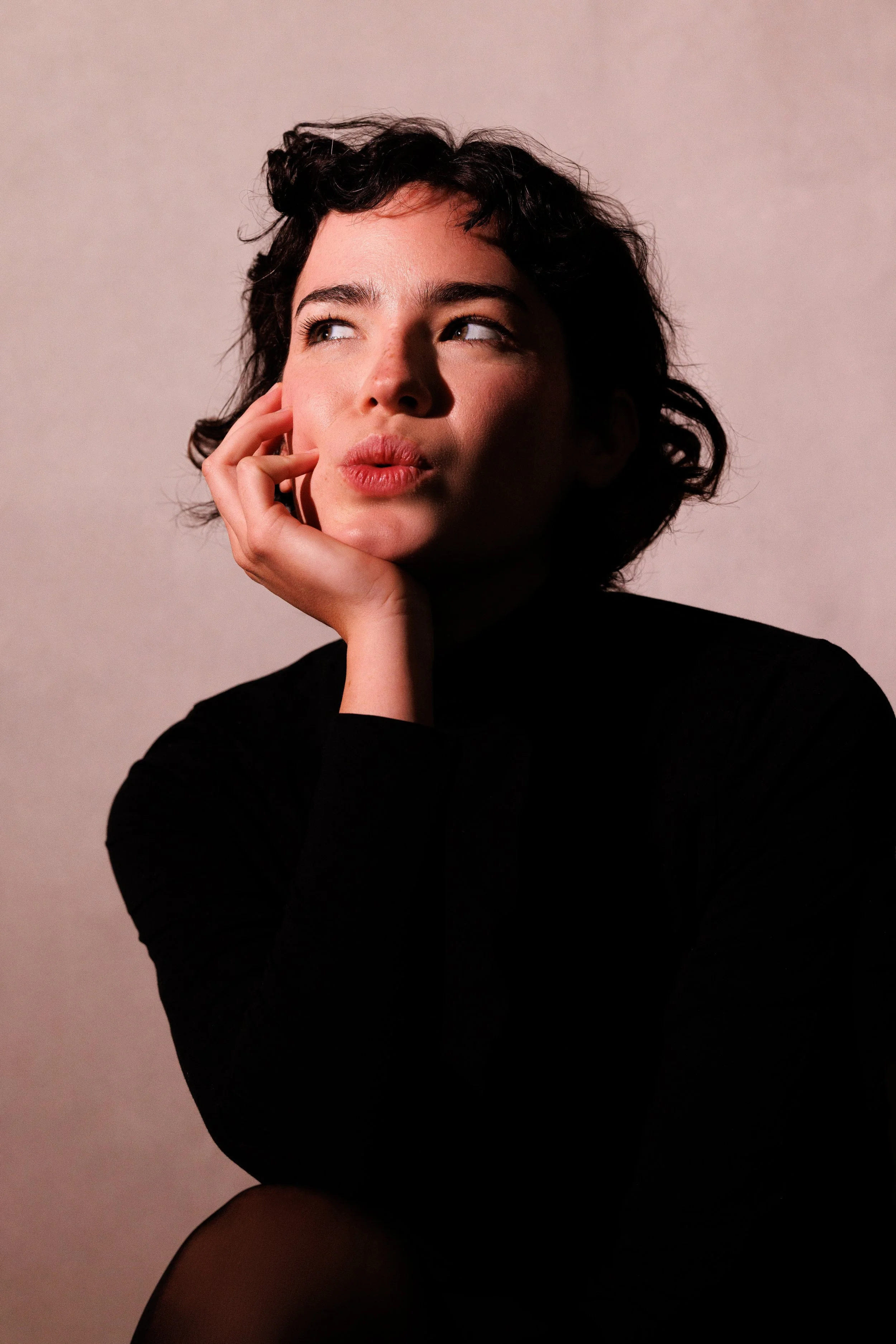 Thoughtful woman with curly hair, hand on chin, looking up