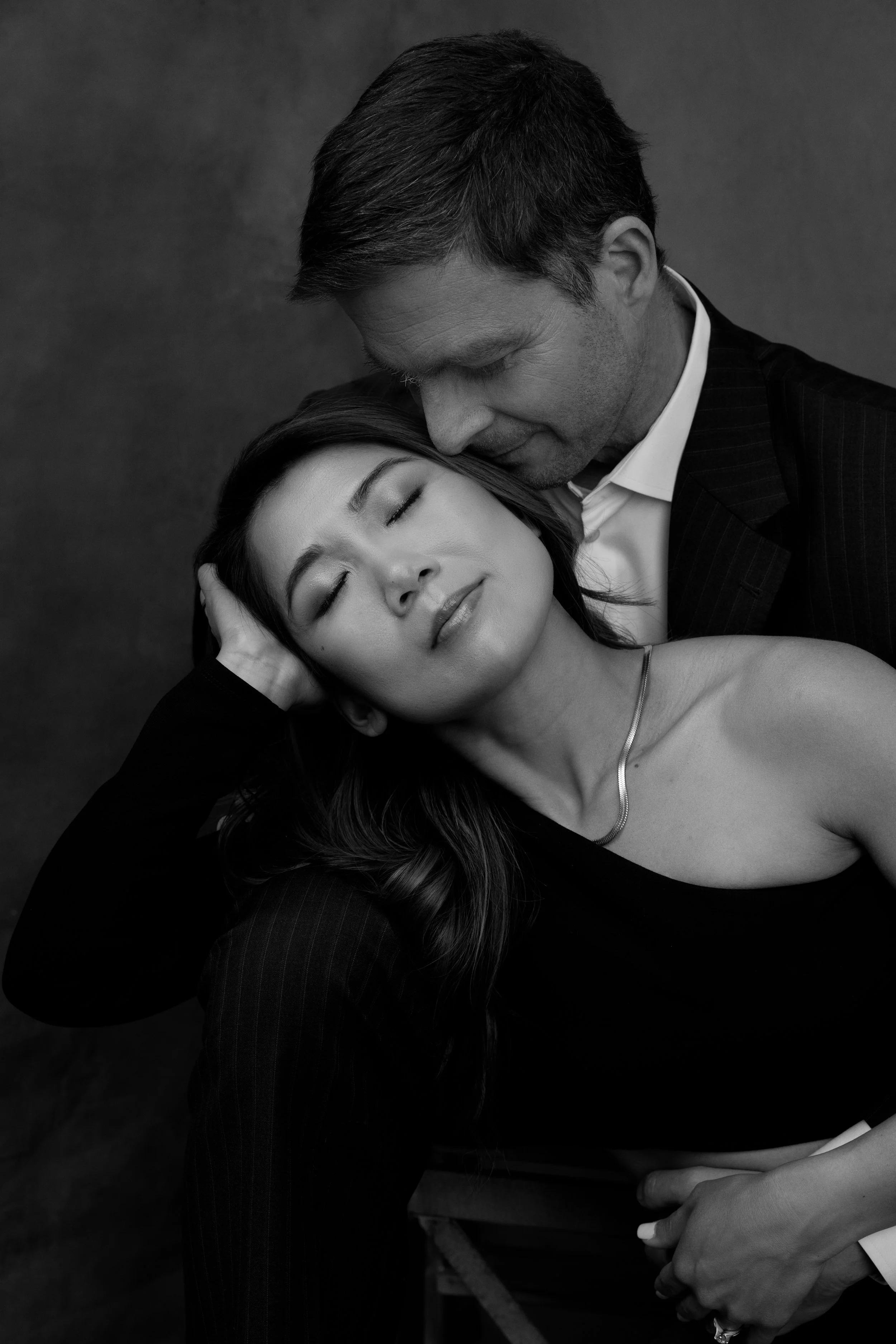 Black and white photo of a couple embracing, woman leaning back with eyes closed, man behind her, looking down.