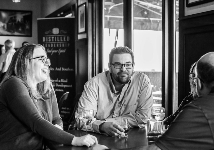 Black and white photo of people having a casual conversation in a bar or café, with glasses of drinks on the table.