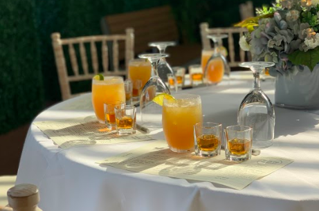Table set with cocktails, shot glasses, wine glasses, and a floral centerpiece on a white tablecloth.
