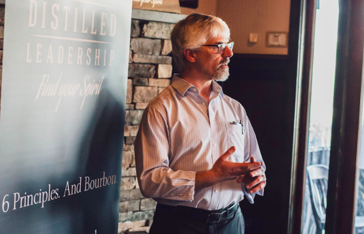 Man speaking next to a "Distilled Leadership" banner in a room with stone walls.