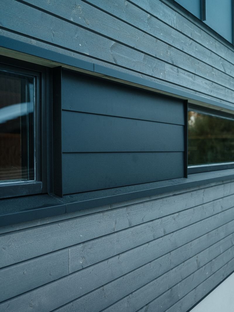 Close-up of a modern building's exterior with horizontal wooden siding painted dark blue, featuring a small rectangular window with a black frame.