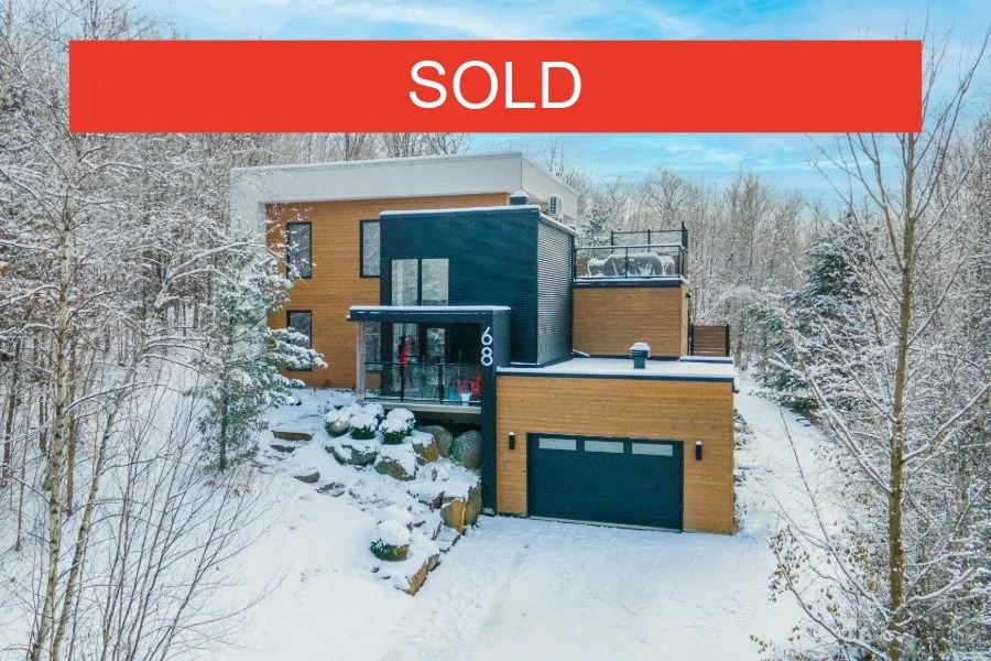 Modern house with a wooden and dark exterior, situated on snow-covered landscape, with a red 'SOLD' banner across the top.
