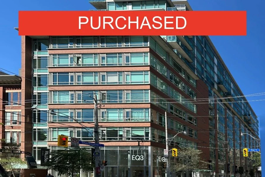 Modern multi-story building with glass windows, located at a street corner with traffic lights, street signs, and pedestrians in front. The photo shows a clear blue sky, and a red banner with the word 'SOLD' across the top.