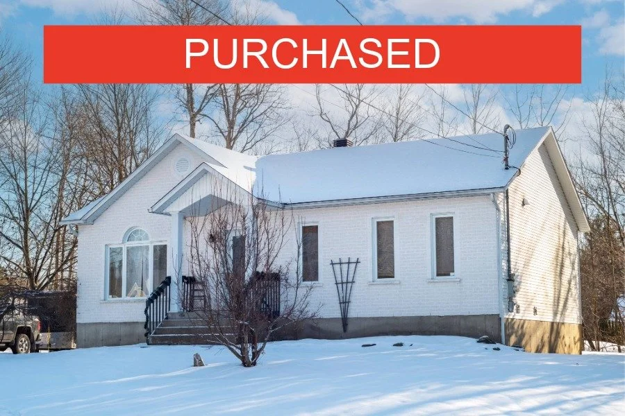 A white house with a snow-covered roof and a 'PURCHASED' banner across the top.