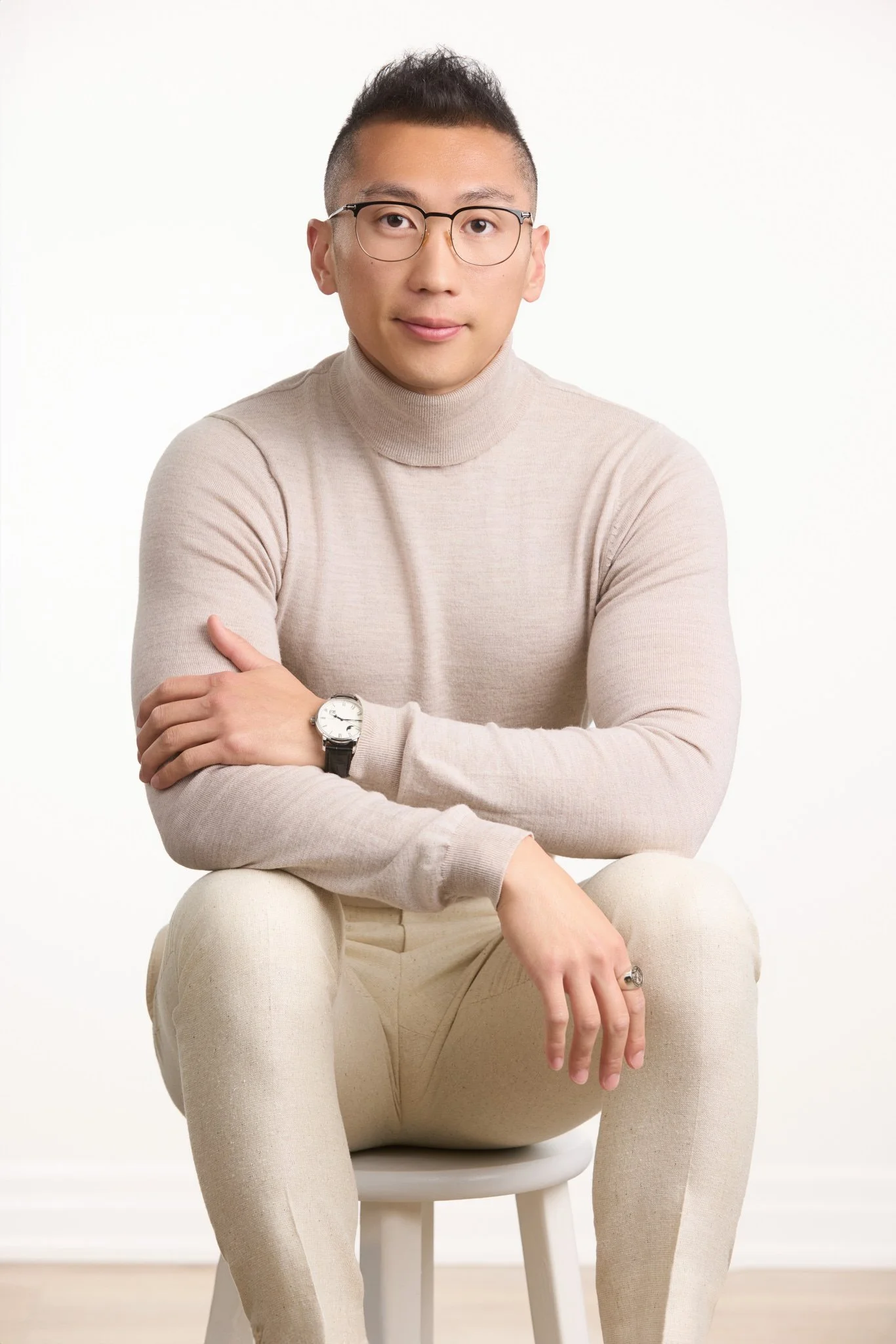 Seated executive portrait of a man in a beige turtleneck on a clean white studio background.