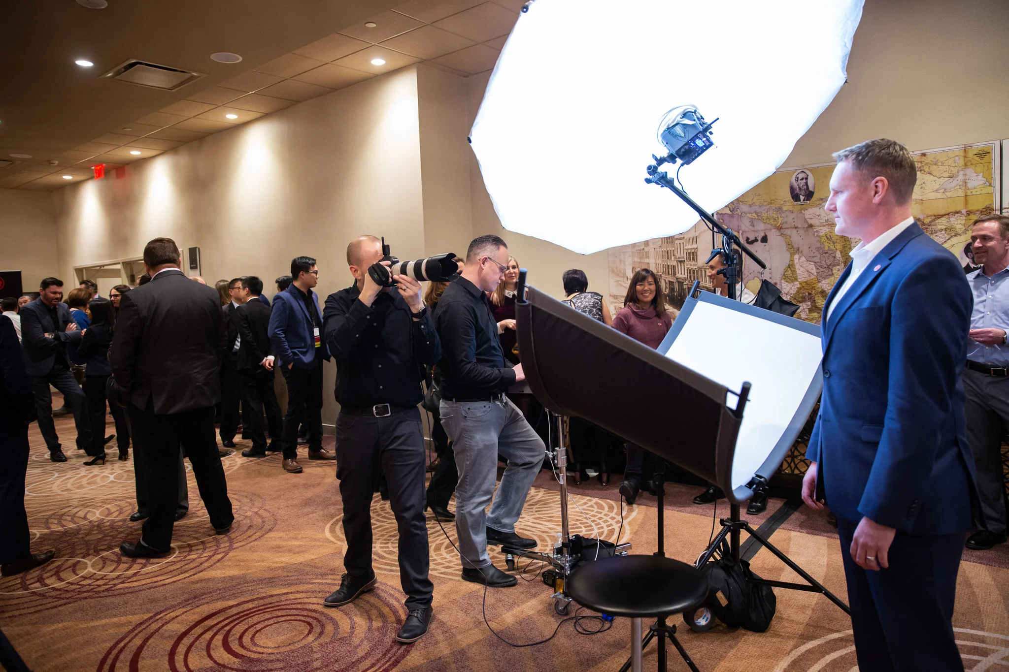 A professional photographer captures an attendee’s headshot at a branded event booth while guests gather in the background.