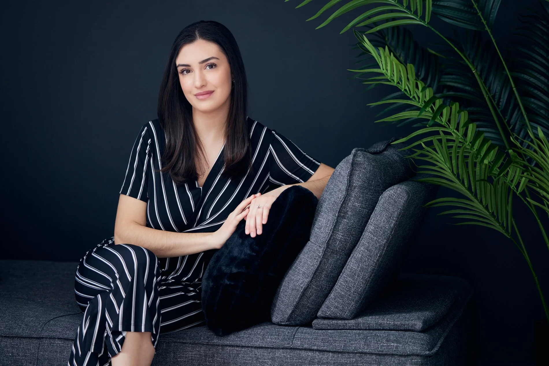 Relaxed business portrait of a woman seated in a modern lounge with greenery.