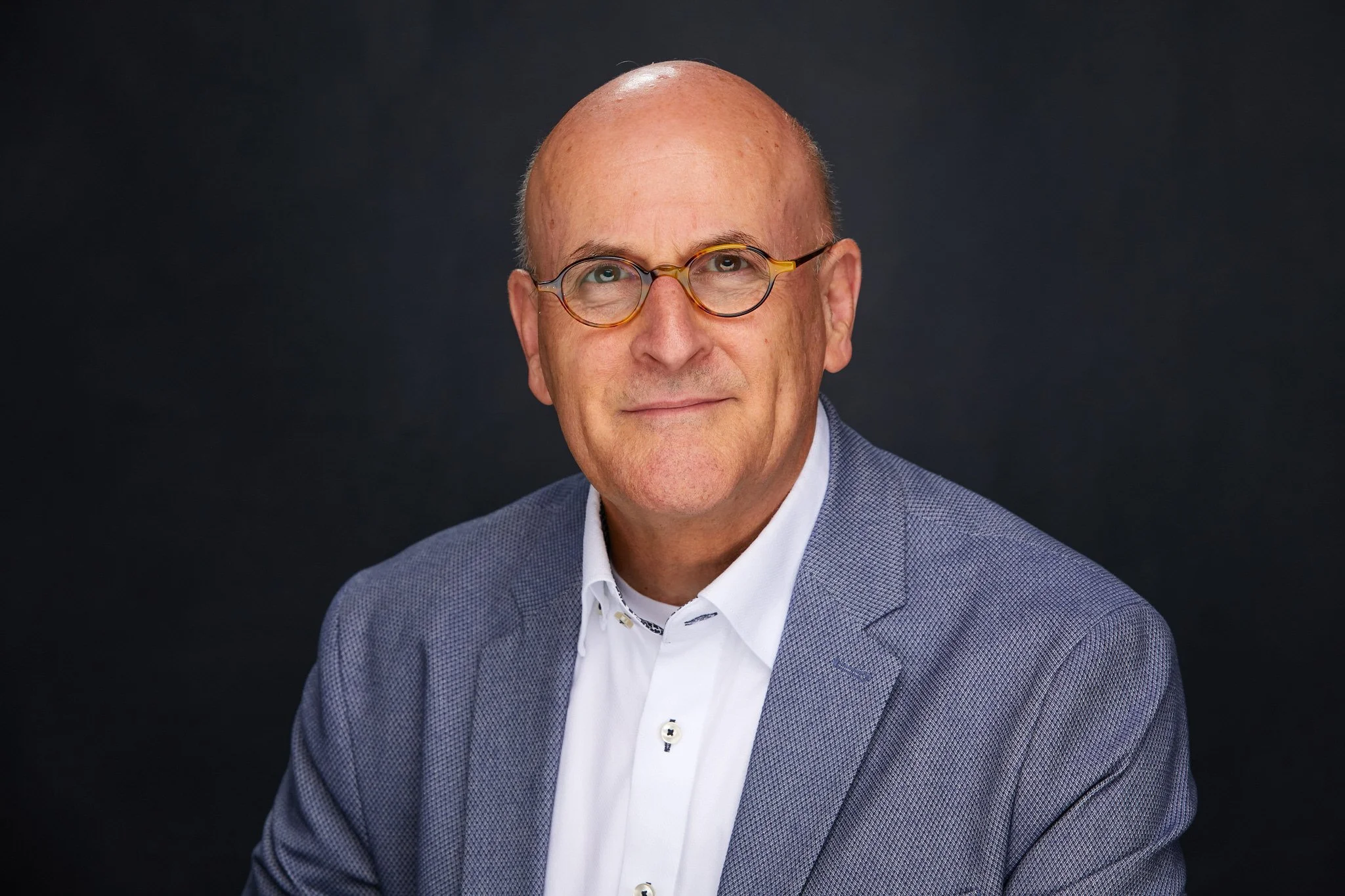 Professional headshot of Steve in a light blazer against a dark studio background.