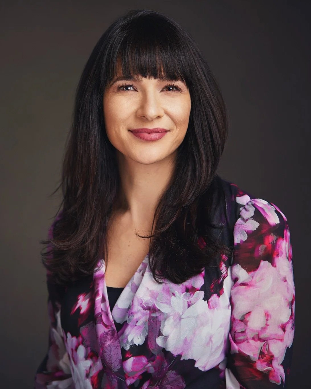 Professional business portrait of a woman in a floral blazer against a dark studio backdrop.
