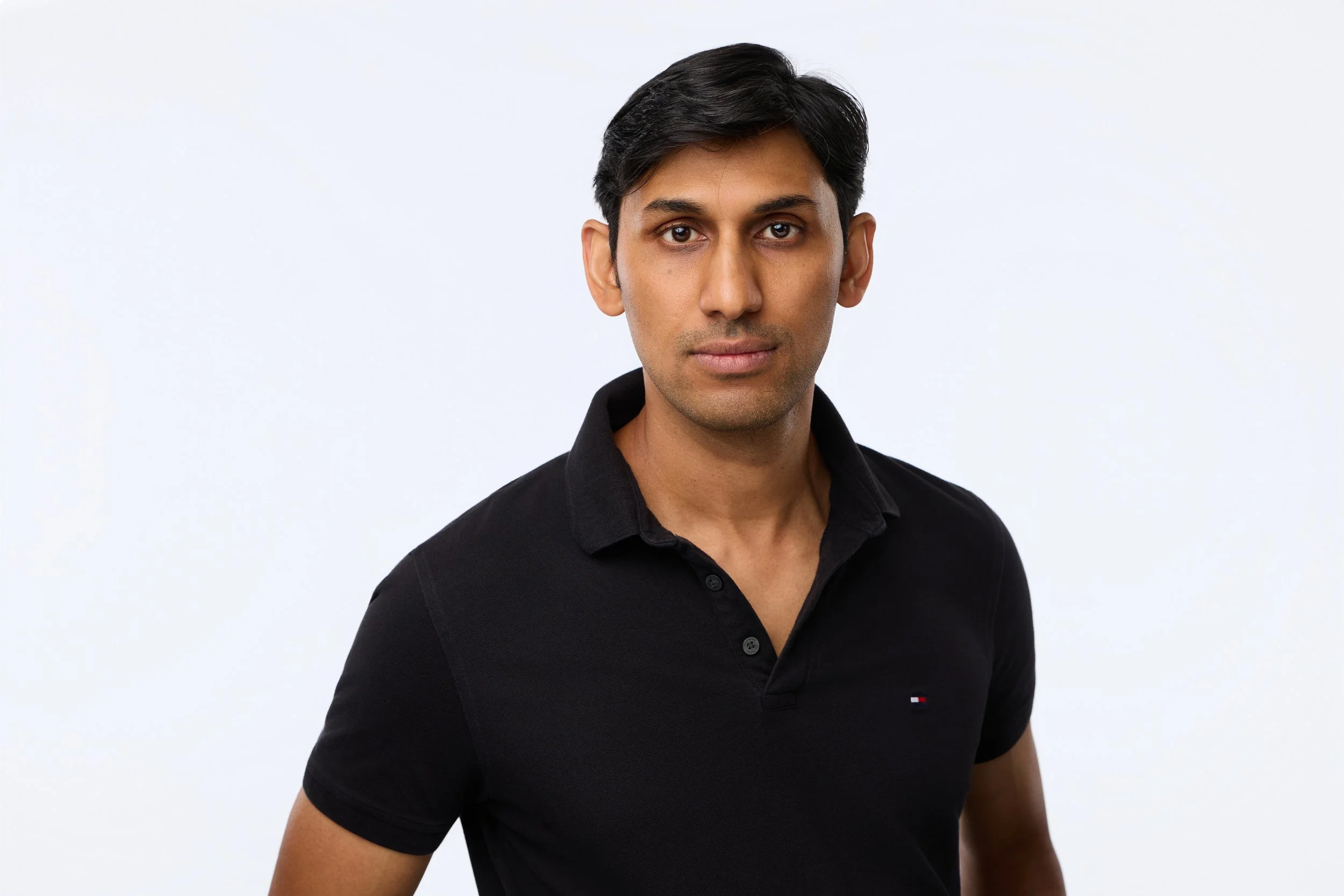 Corporate headshot of a dark-haired man wearing a black polo shirt with a neutral expression.