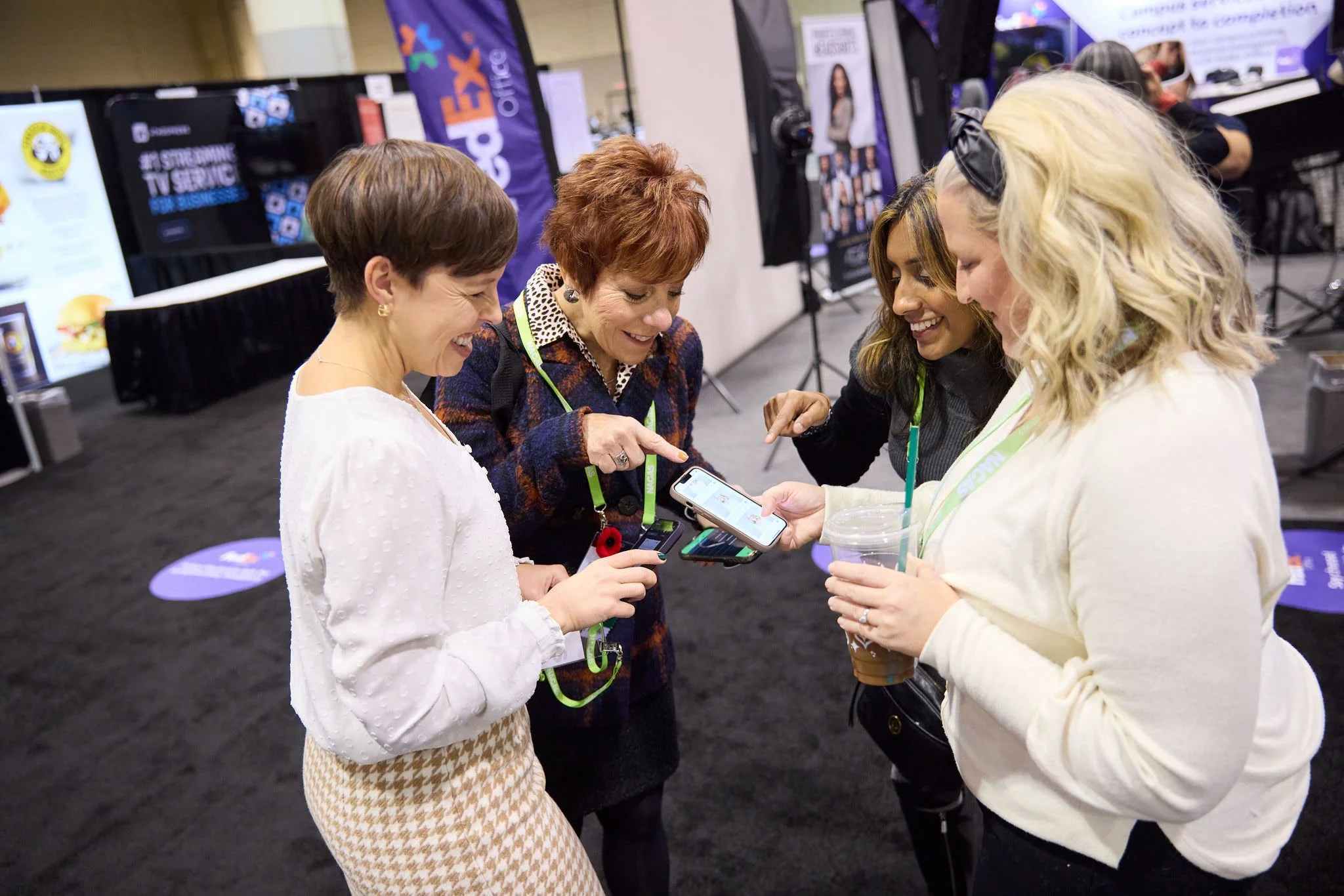 Four women looking at their phone to see instantly delivered headshots from FedEx Office.