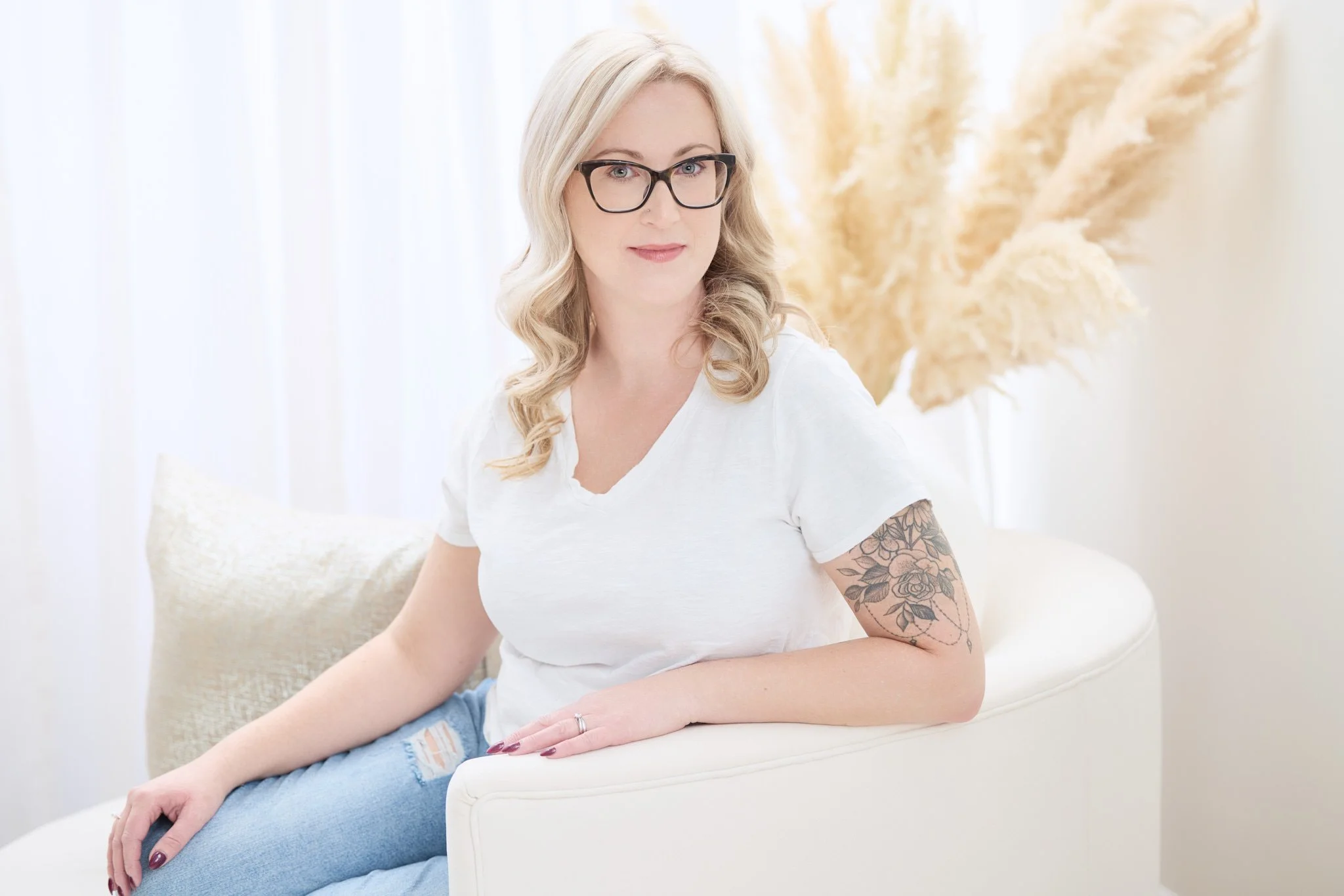 Relaxed personal branding portrait of a woman seated in a bright neutral studio.