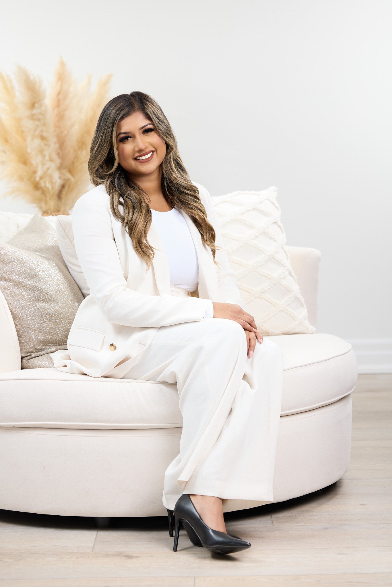 Elegant professional branding portrait of a woman in a white suit seated in a bright studio.