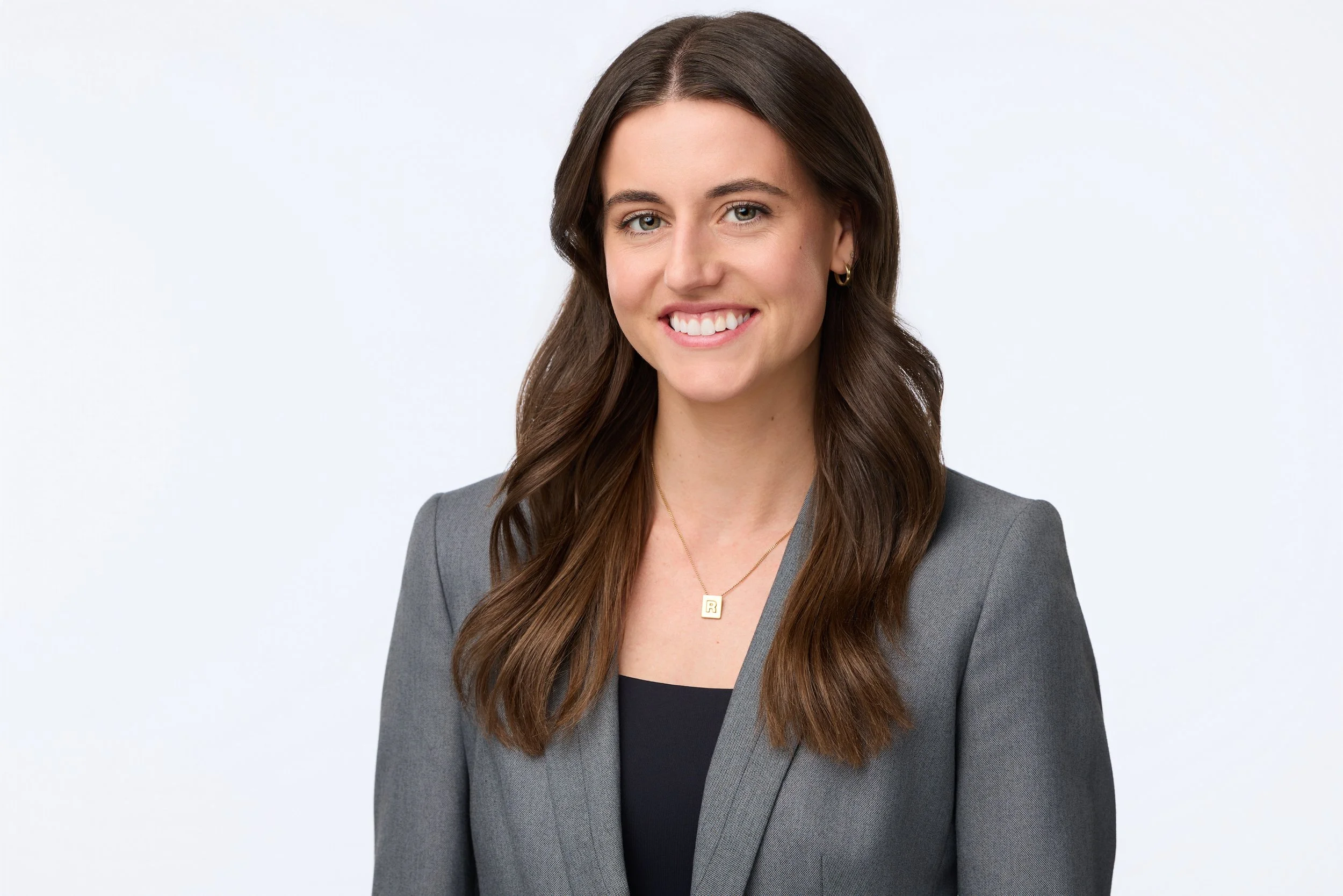 Modern business portrait of a brown-haired woman wearing a grey blazer against a neutral background.