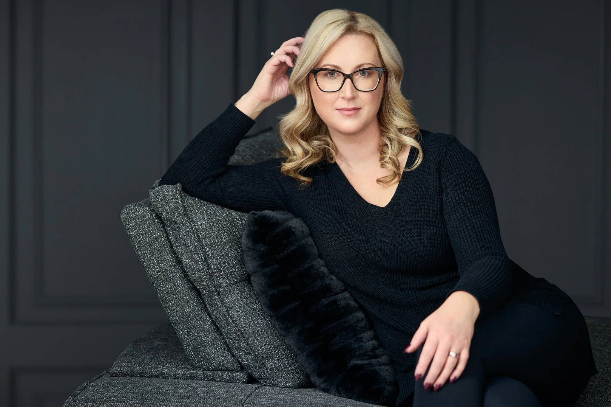 Personal branding portrait of a woman dressed in black and seated against a dark studio background.