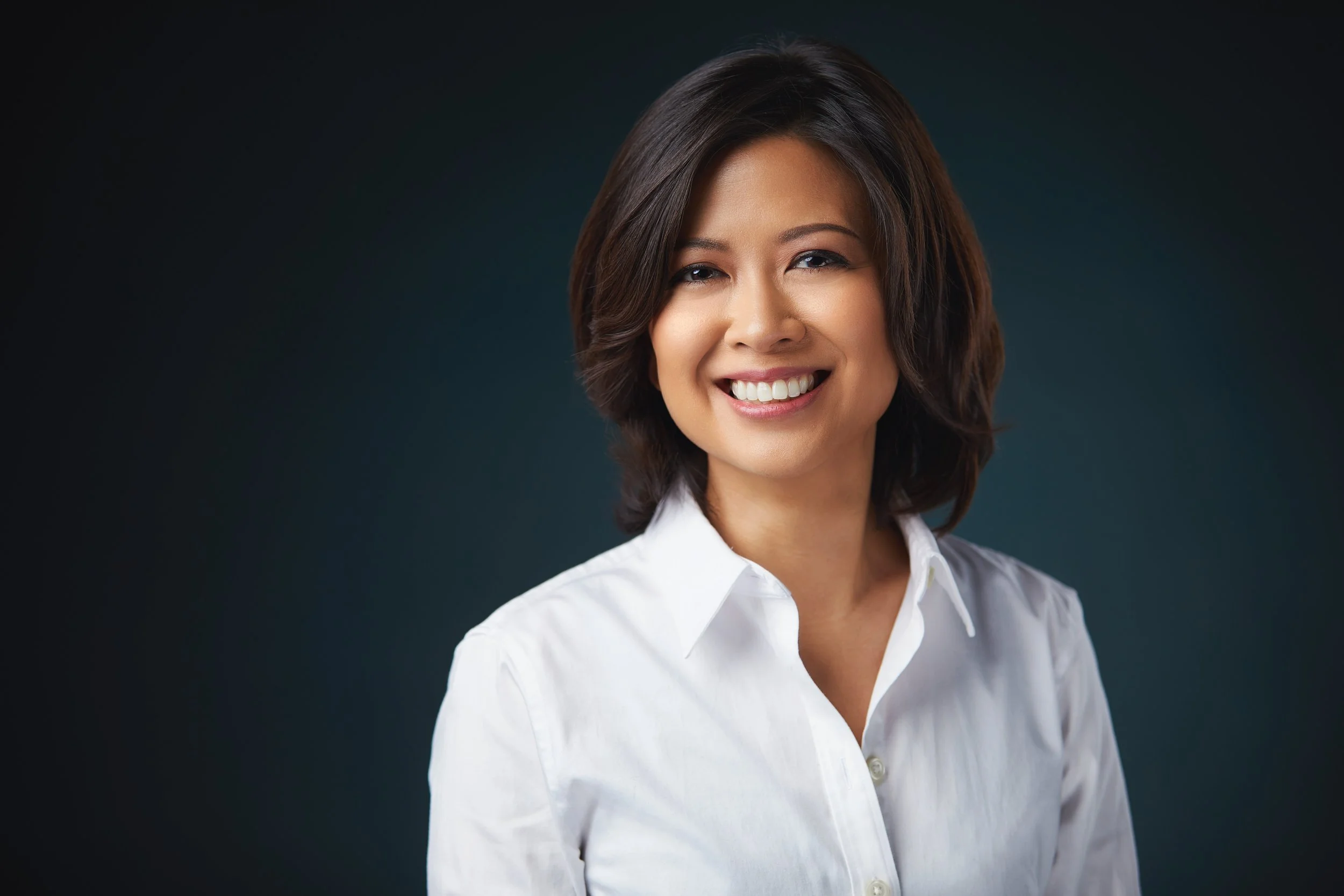 Professional headshot of Annie in a white blouse against a dark studio background.