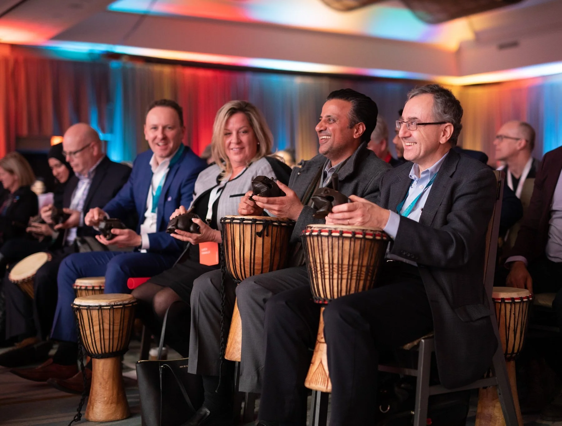 Corporate event guests smile and play hand drums together during an interactive group activity.