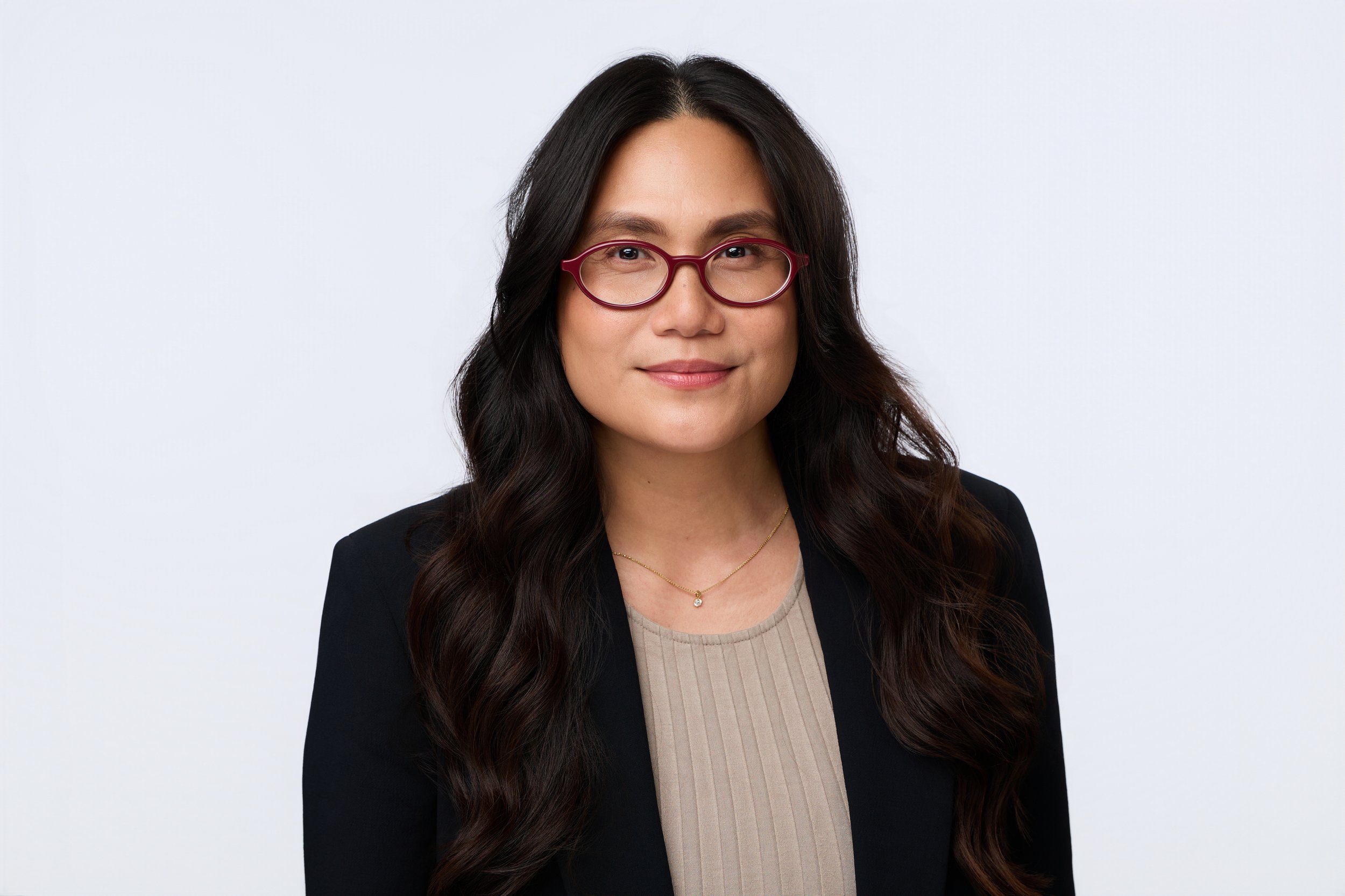 Executive portrait of a dark-haired woman wearing red glasses and a black blazer.
