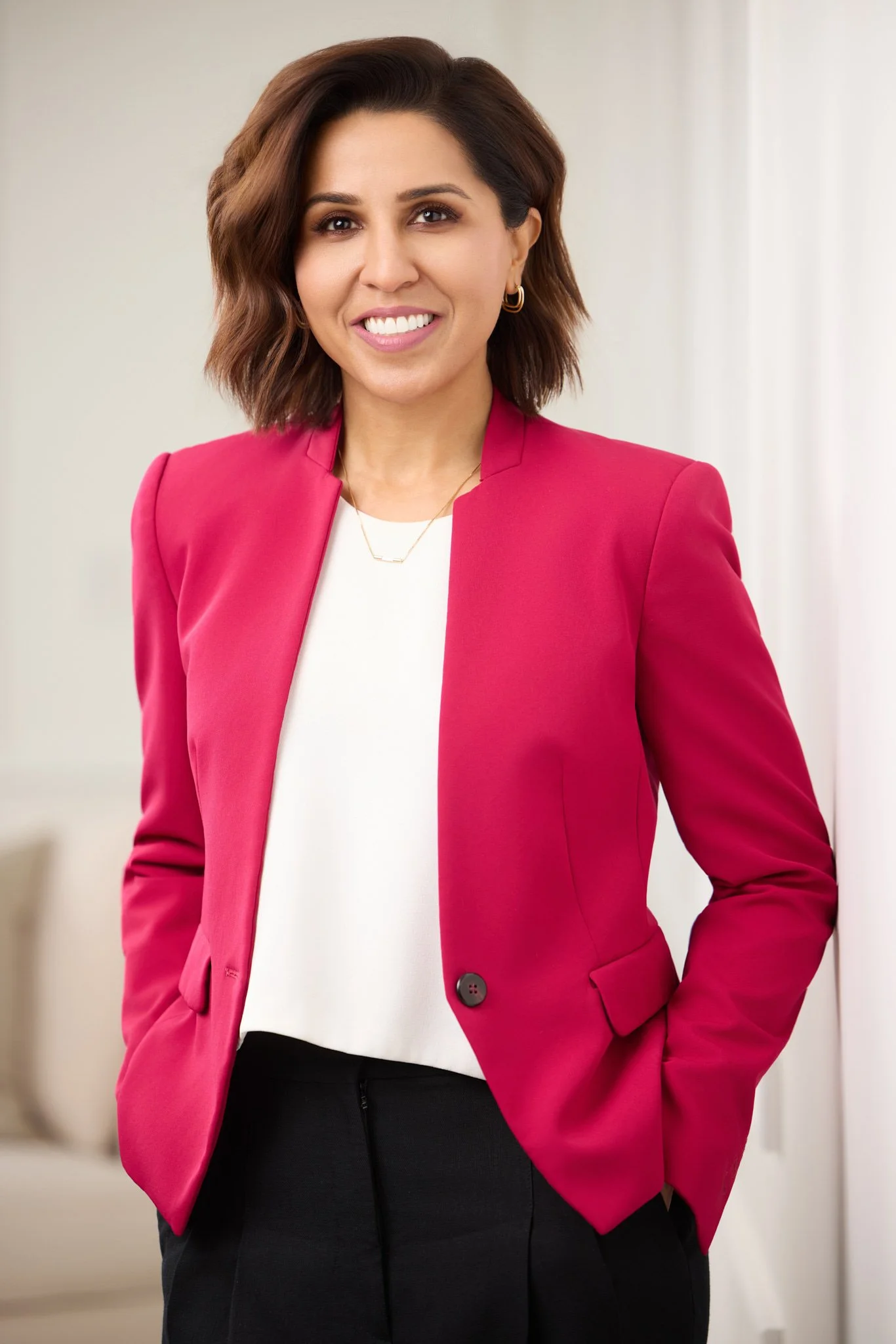 Confident executive business portrait of a woman in a pink blazer against a bright neutral background.