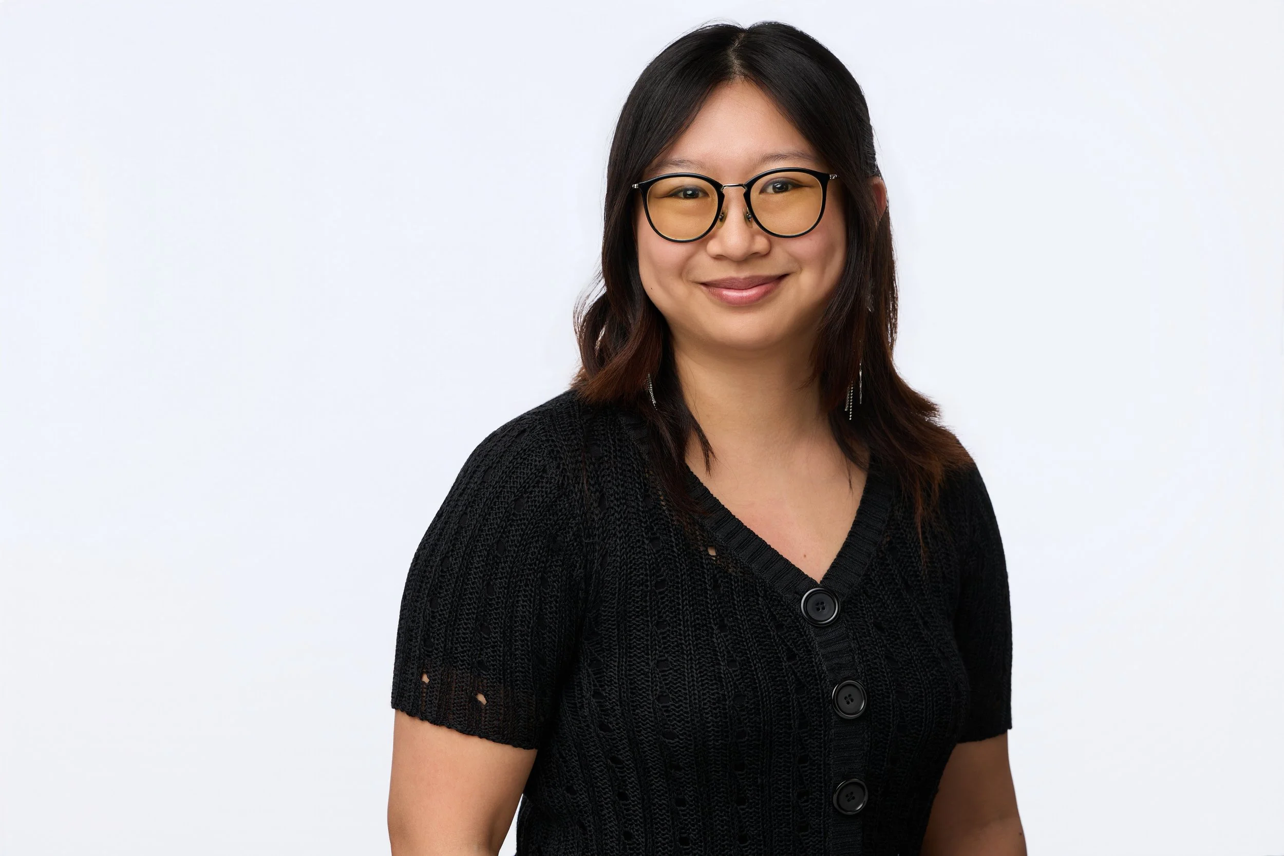 Business portrait of a dark-haired woman wearing black glasses and a dark shirt, smiling at the camera.