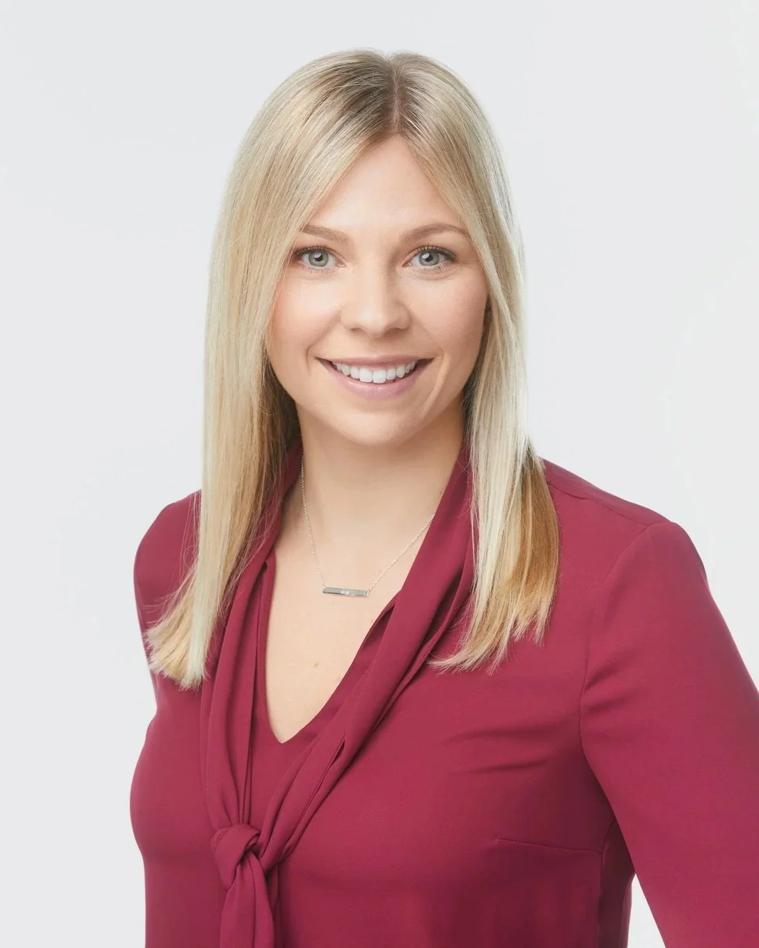 Professional business headshot of a smiling woman in a red shirt against a light grey studio background.