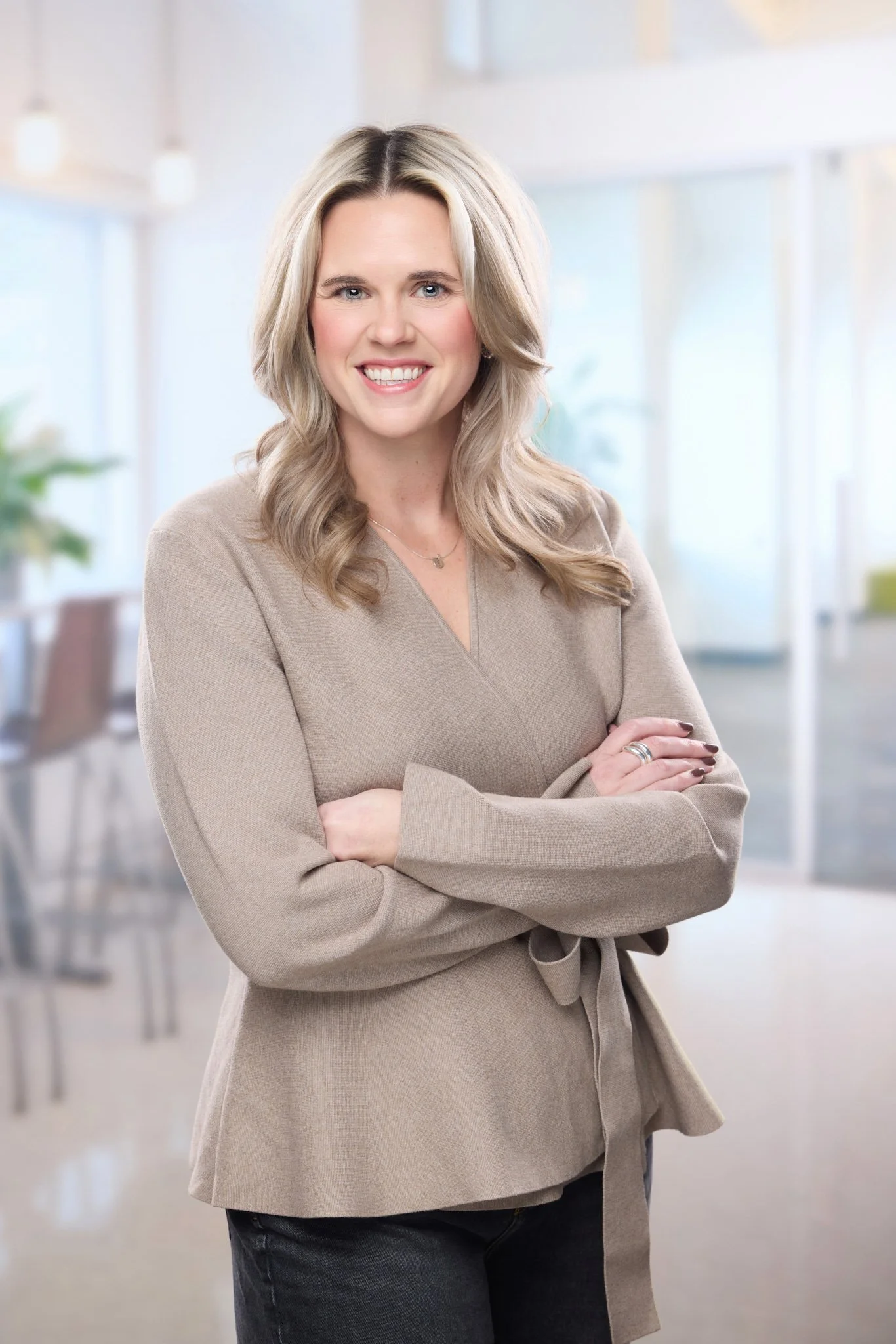 Executive business portrait of a smiling woman with her arms crossed in a modern office.